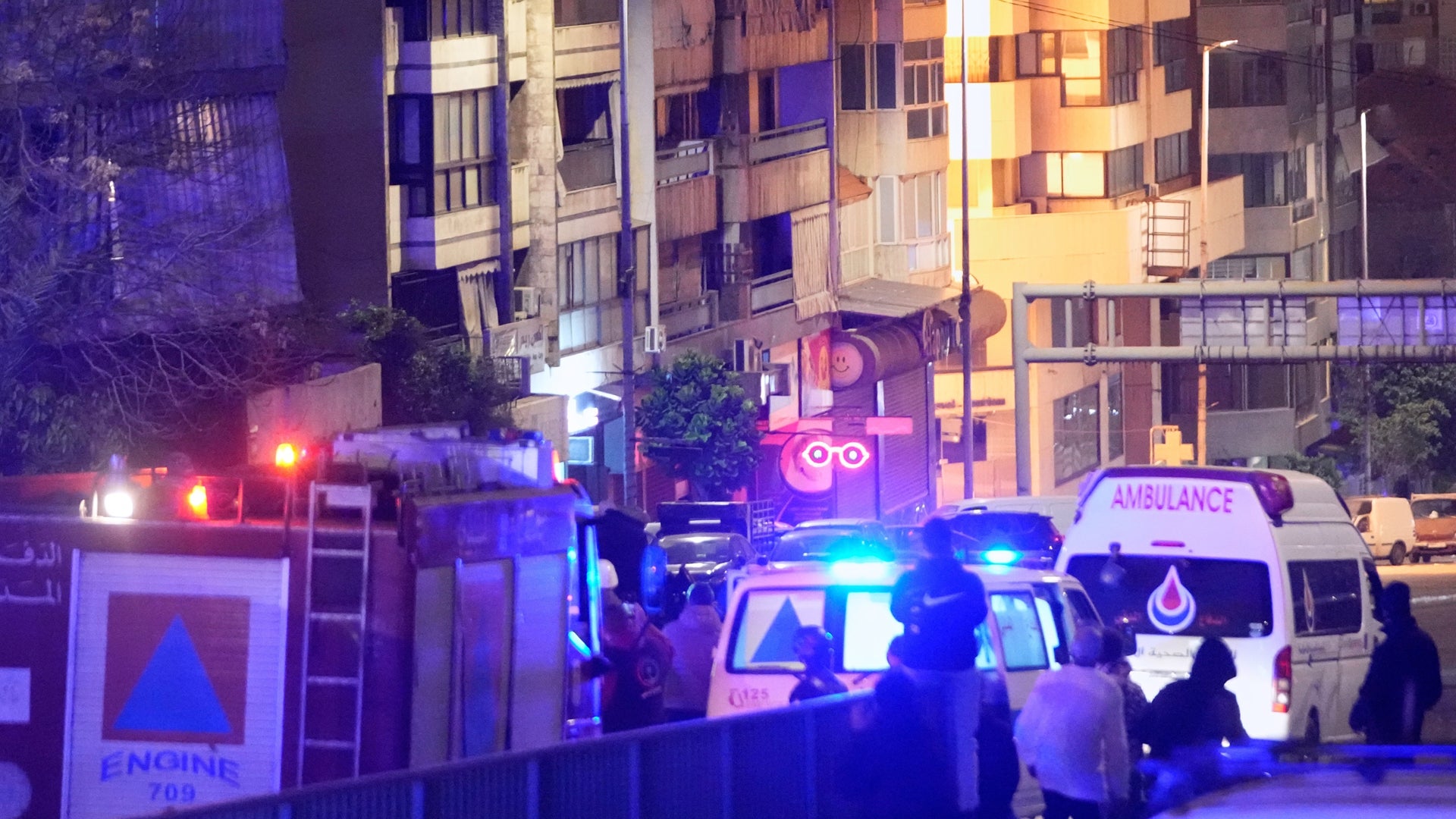 Nattlig scen med brandbilar och ambulanser på en stadsgata omgiven av bostadshus.