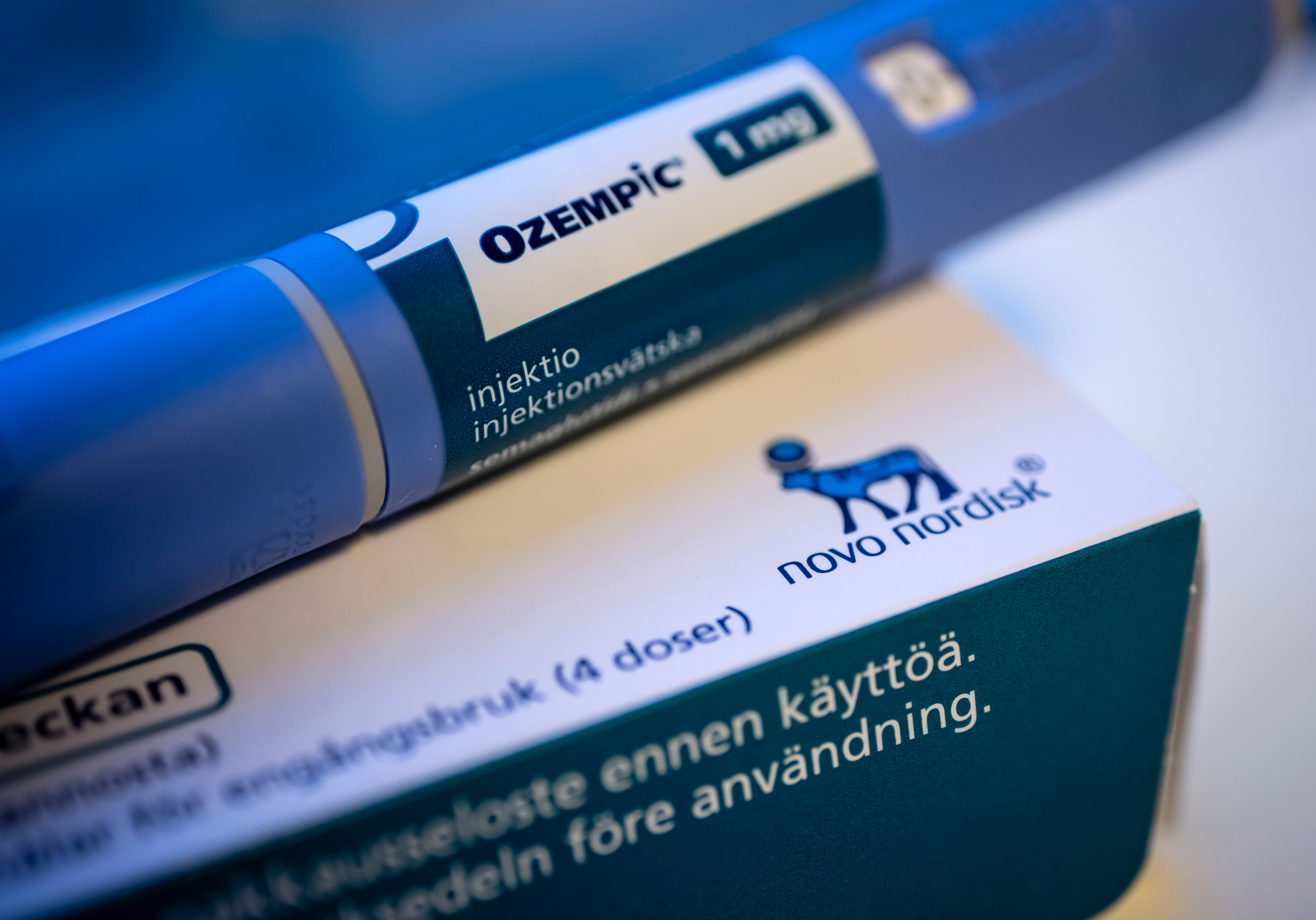Ozempic injektionspenna i blå färg med vit etikett, placerad bredvid förpackningsmaterial från Novo Nordisk.