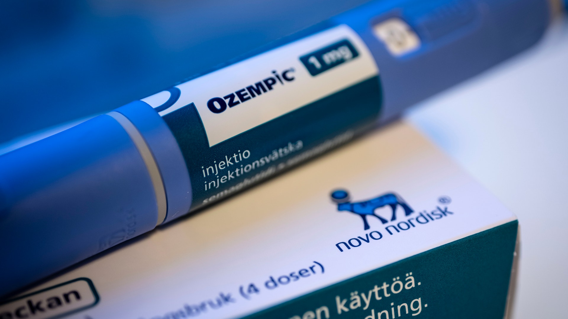 Ozempic injektionspenna i blå färg med vit etikett, placerad bredvid förpackningsmaterial från Novo Nordisk.