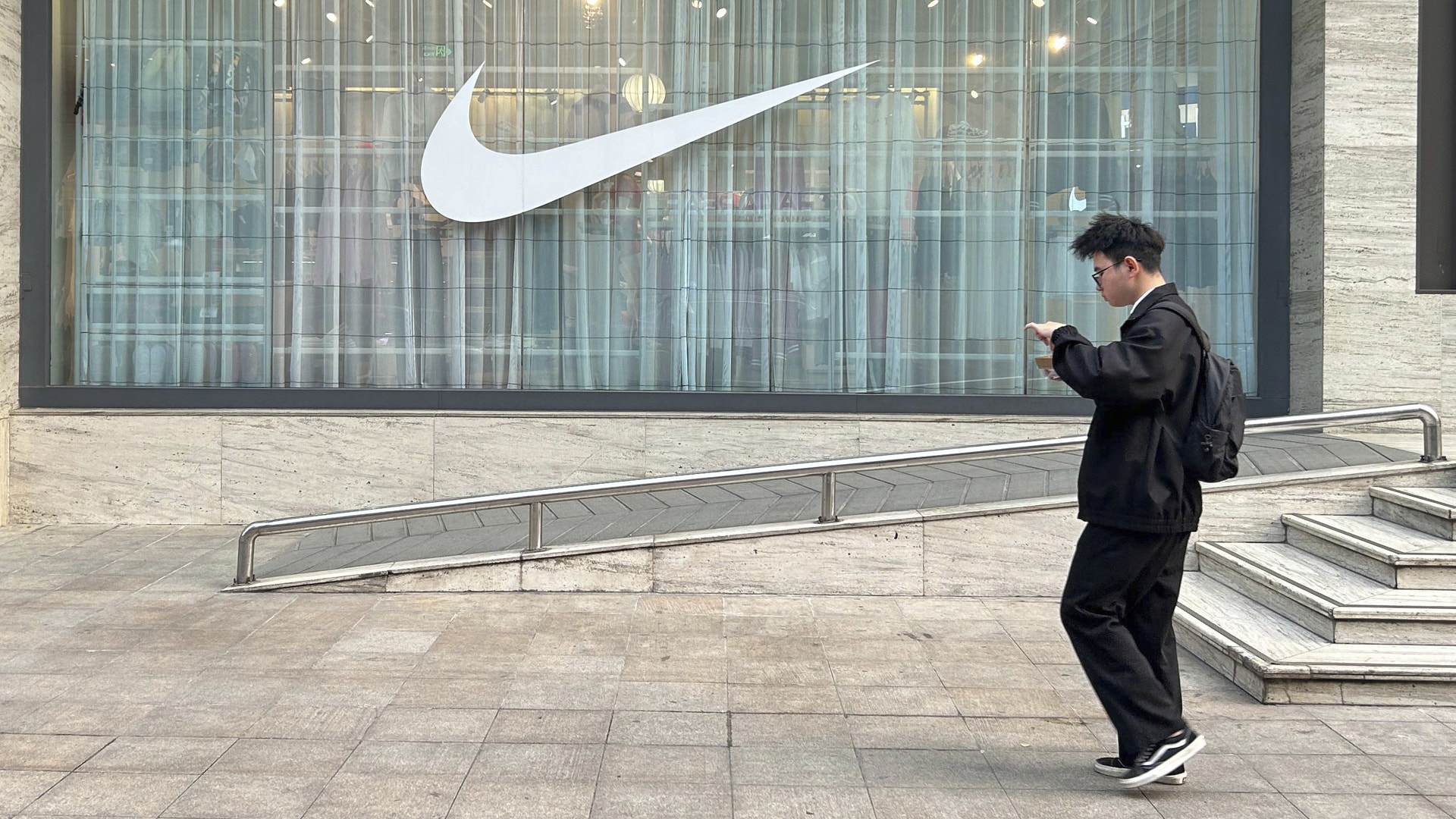 En person går förbi en Nike-butik med stort Nike-emblem i skyltfönstret.