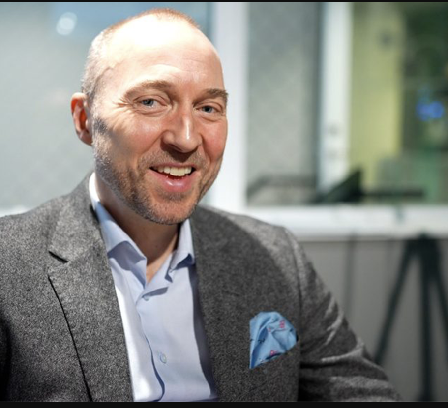 Porträttfoto av en man i grå kavaj och ljusblå skjorta som ler mot kameran.