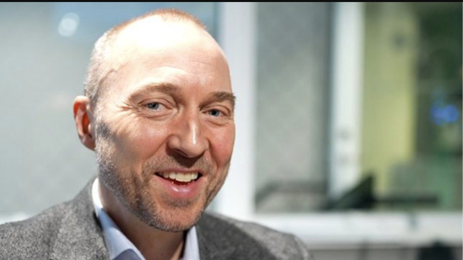 Porträttfoto av en man i grå kavaj och ljusblå skjorta som ler mot kameran.