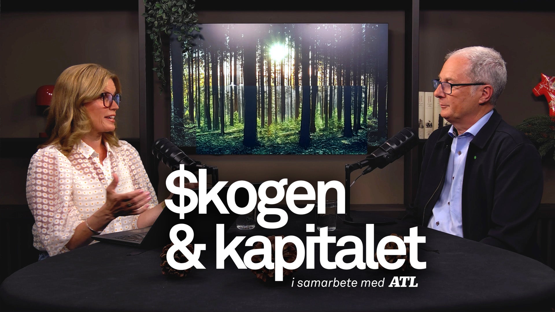 Två personer sitter vid ett bord och diskuterar framför en skärm som visar en grön skog. Texten 'Skogen & kapitalet' visas i förgrunden.