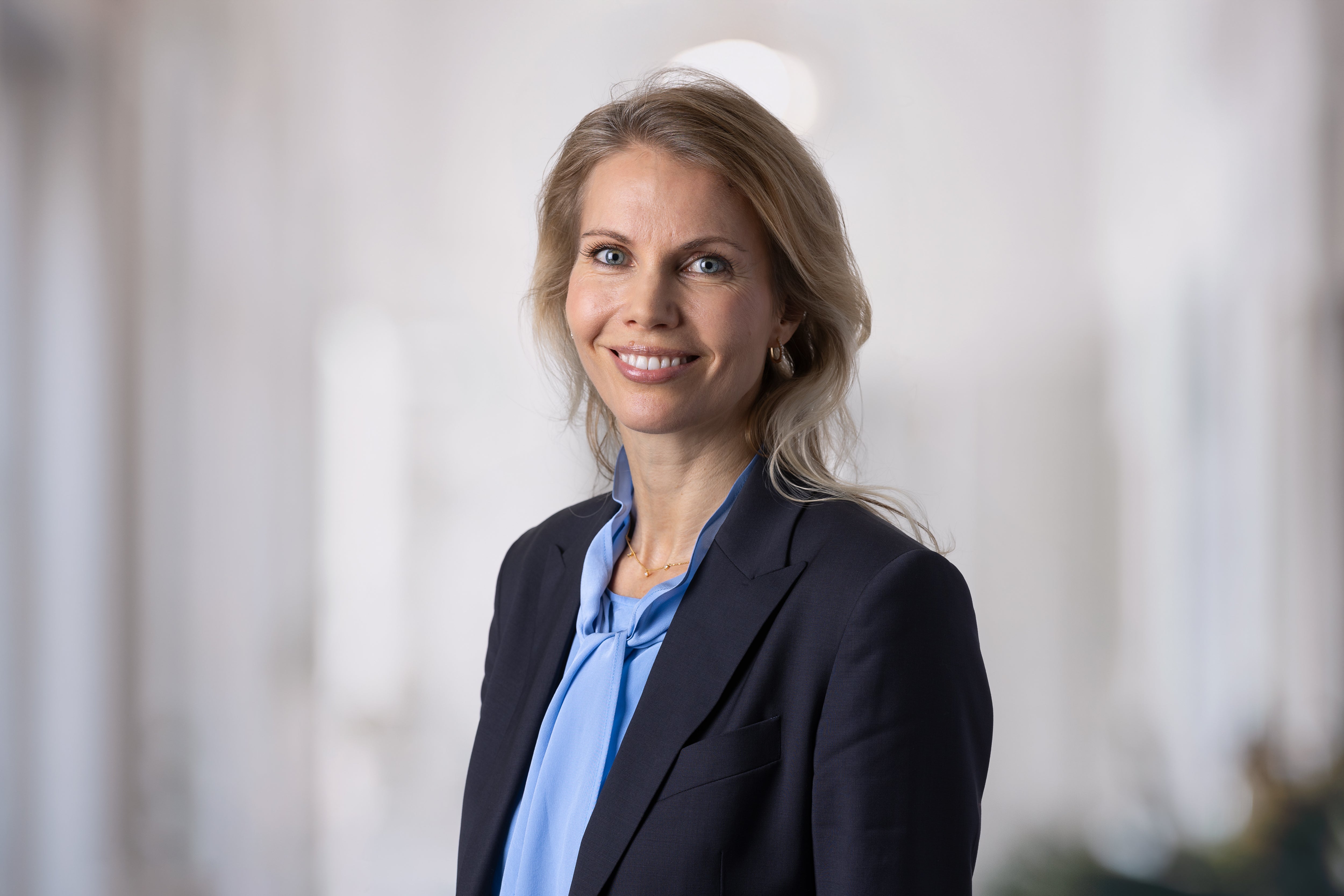 Porträtt av en leende kvinna i professionell klädsel med mörk kavaj och blå blus.