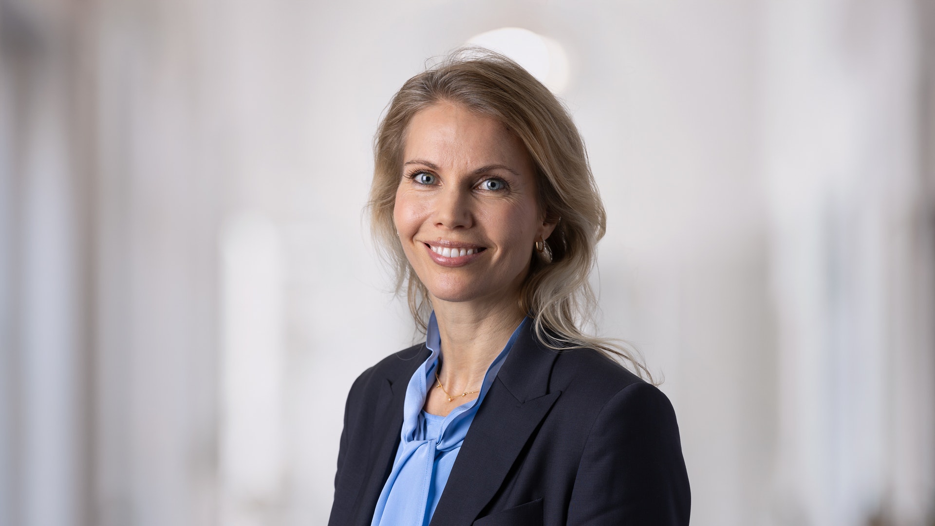 Porträtt av en leende kvinna i professionell klädsel med mörk kavaj och blå blus.