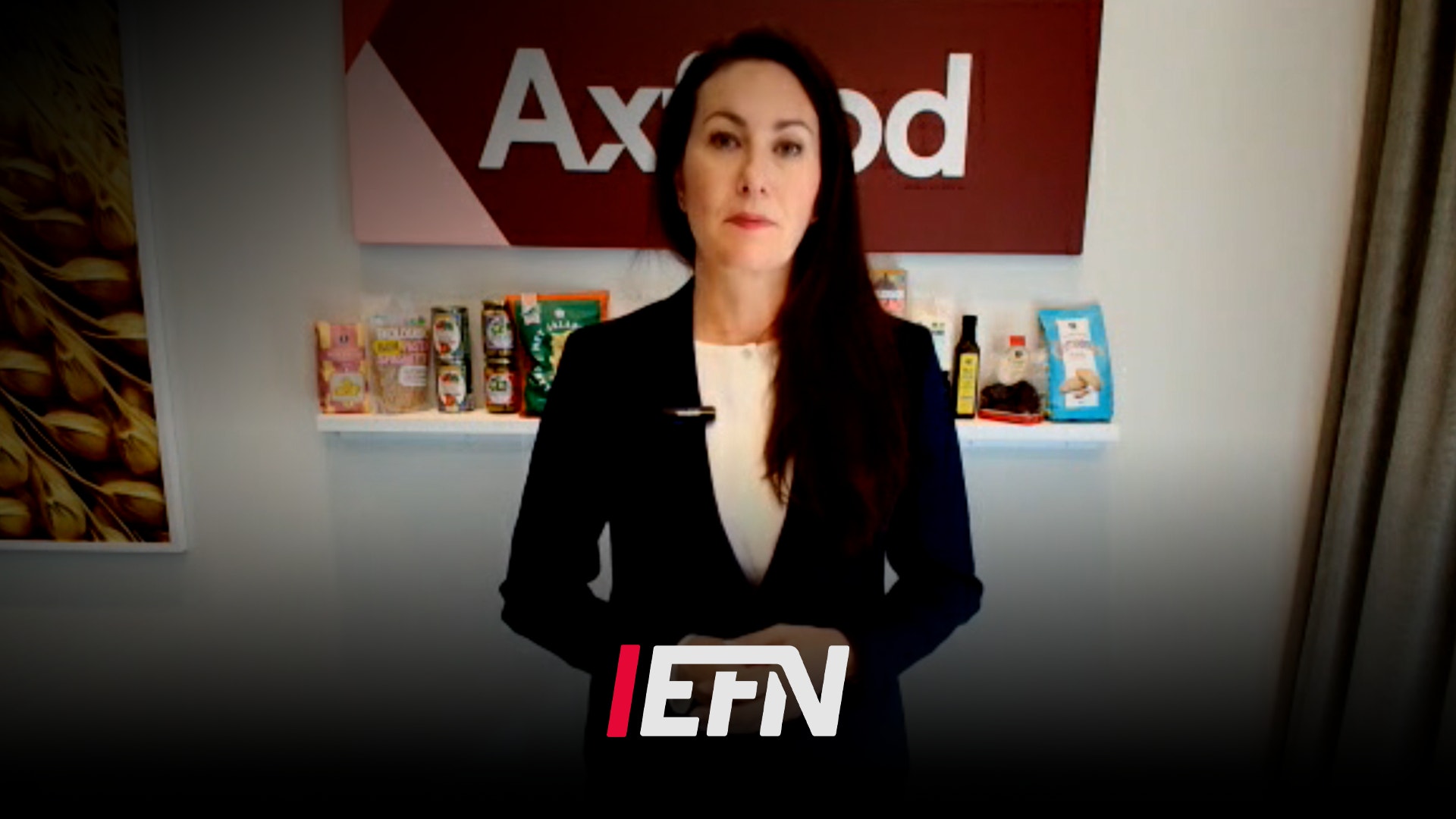 Kvinna i svart blazer står framför en vägg med Axfood-logotypen. Hon håller upp EFN-logotypen framför sig.