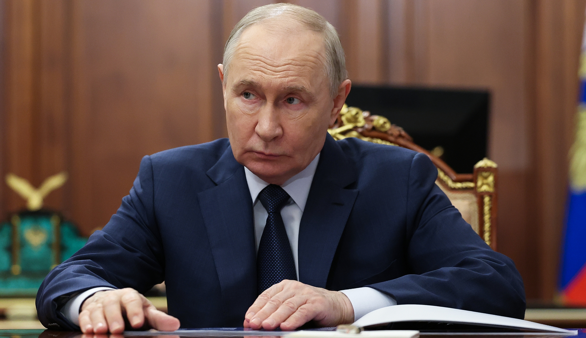 Porträtt av en man i mörkblå kostym och slips vid ett skrivbord i en formell miljö.