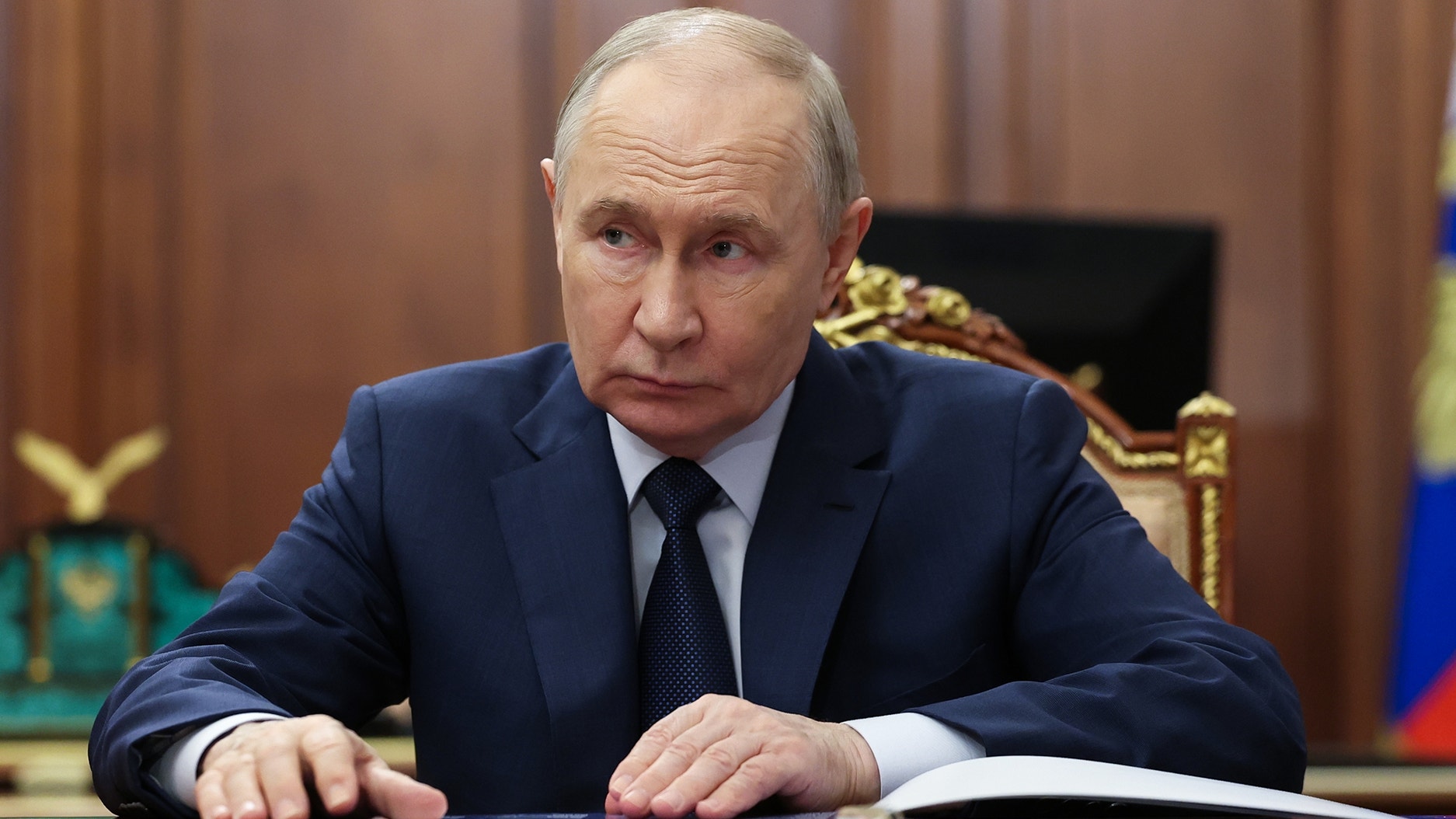 Porträtt av en man i mörkblå kostym och slips vid ett skrivbord i en formell miljö.