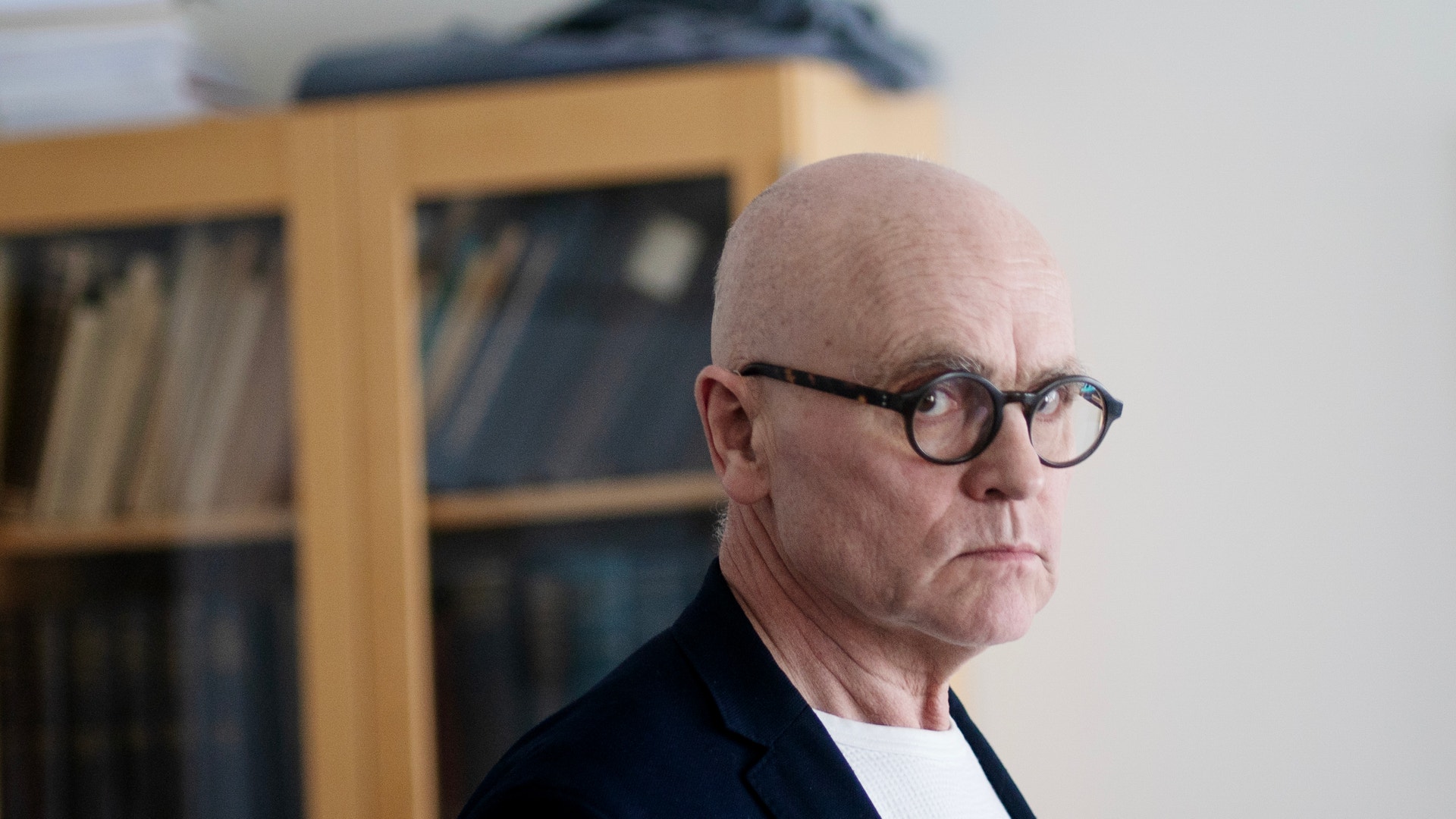 Porträtt av en man med glasögon och mörk kavaj framför en bokhylla