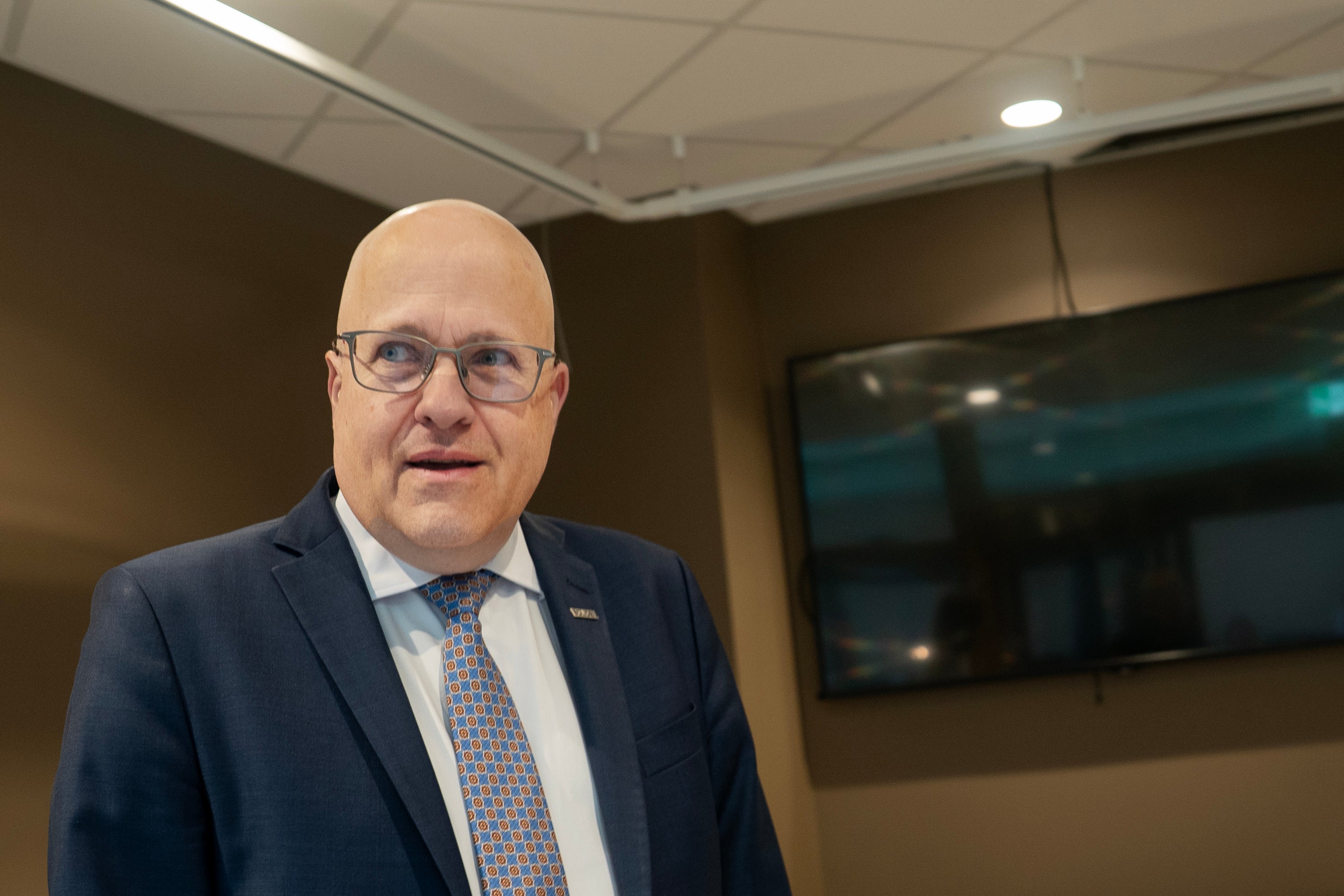 Porträtt av en man i kostym och glasögon som står i ett modernt kontorsrum.