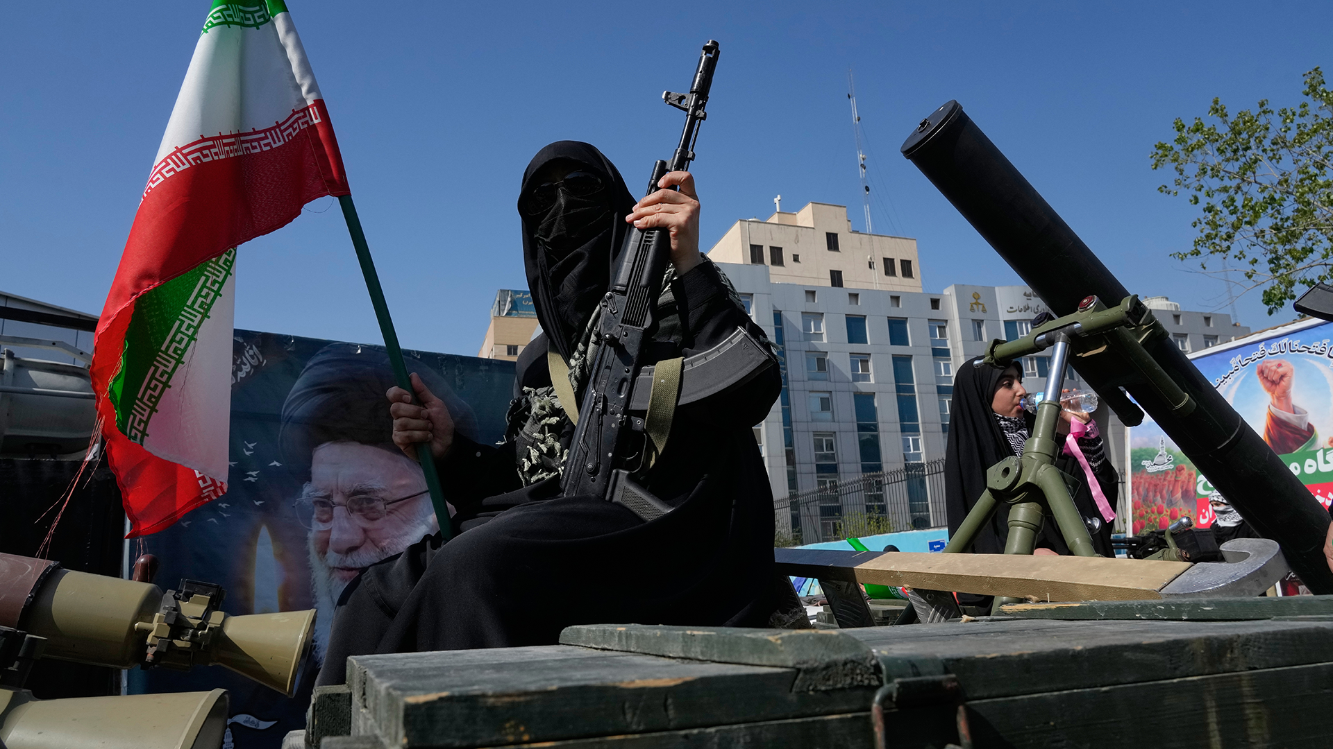 Militär parad i Iran med iransk flagga, soldater med vapen och militär utrustning framför stadshus.