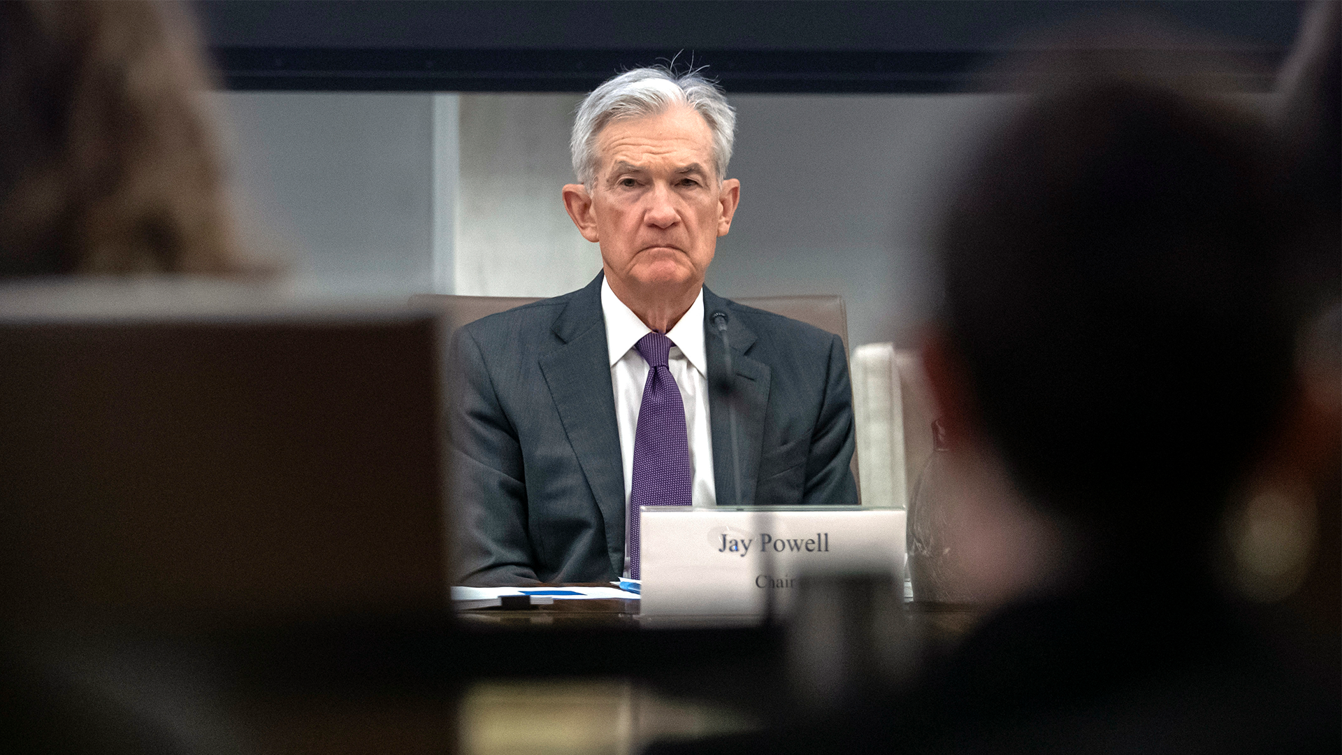 Jerome Powell sitter på en stol på riksbankens presskonfferens. Han har lila slips och grå kostym, och tittar fram mellan bakhuvudena på två journalister i publiken.