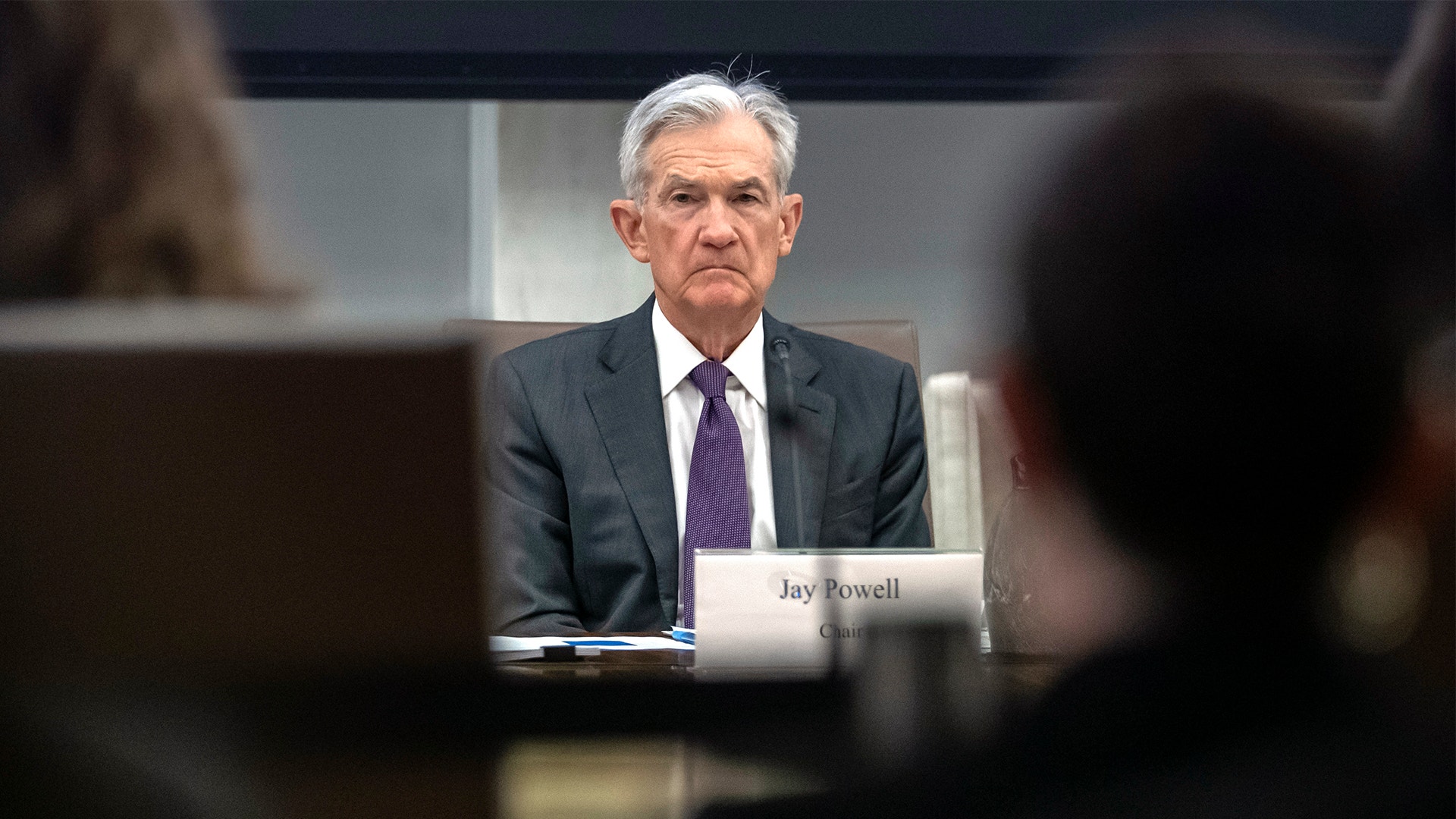 Jerome Powell sitter på en stol på riksbankens presskonfferens. Han har lila slips och grå kostym, och tittar fram mellan bakhuvudena på två journalister i publiken.