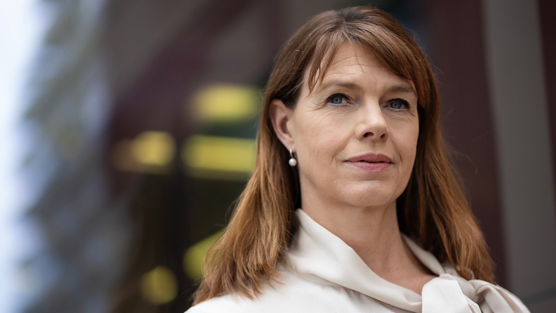 Porträtt av en kvinnlig person med långt rödbrunt hår, klädd i vit skjorta med rosett.