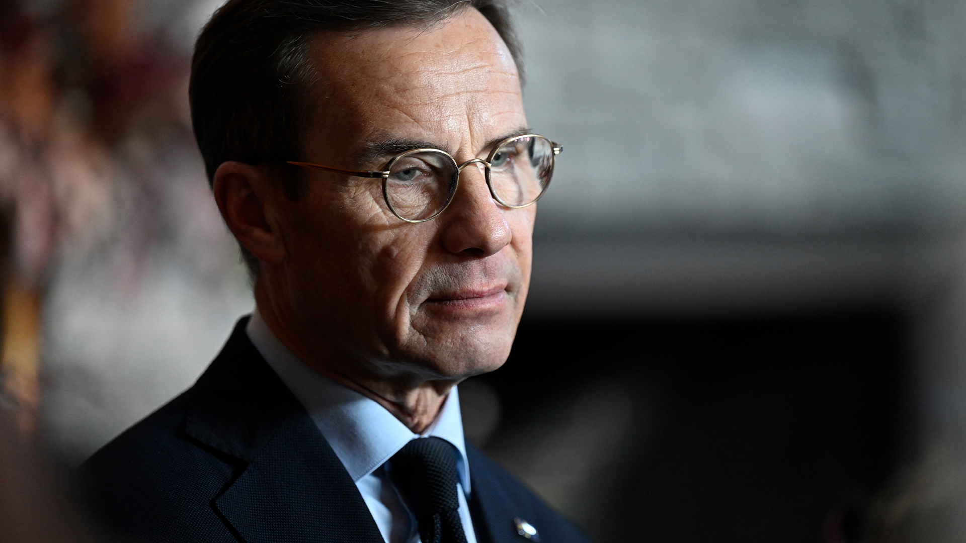 Porträttfoto av en man med glasögon i formell kostym och blå slips.