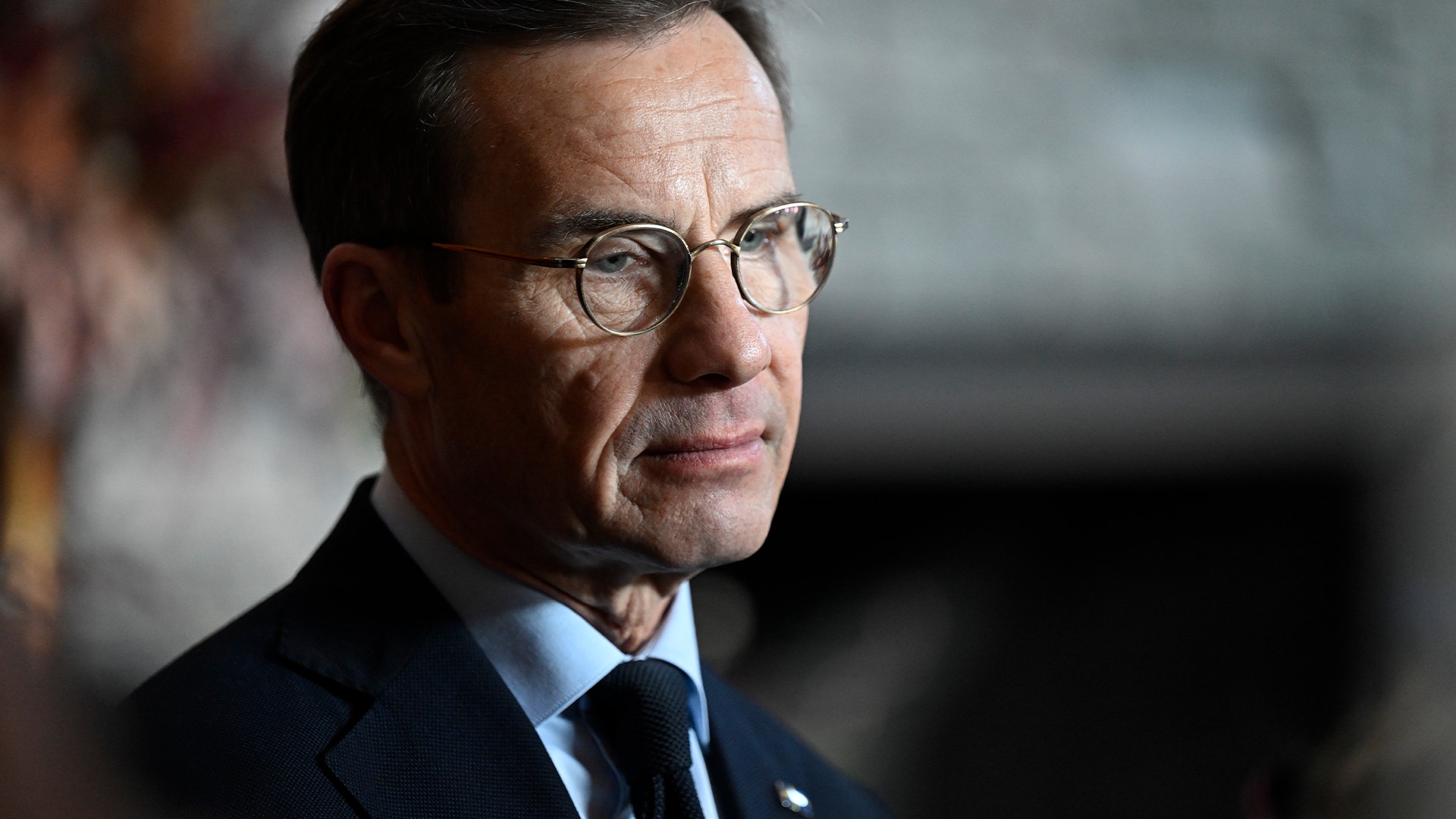 Porträttfoto av en man med glasögon i formell kostym och blå slips.