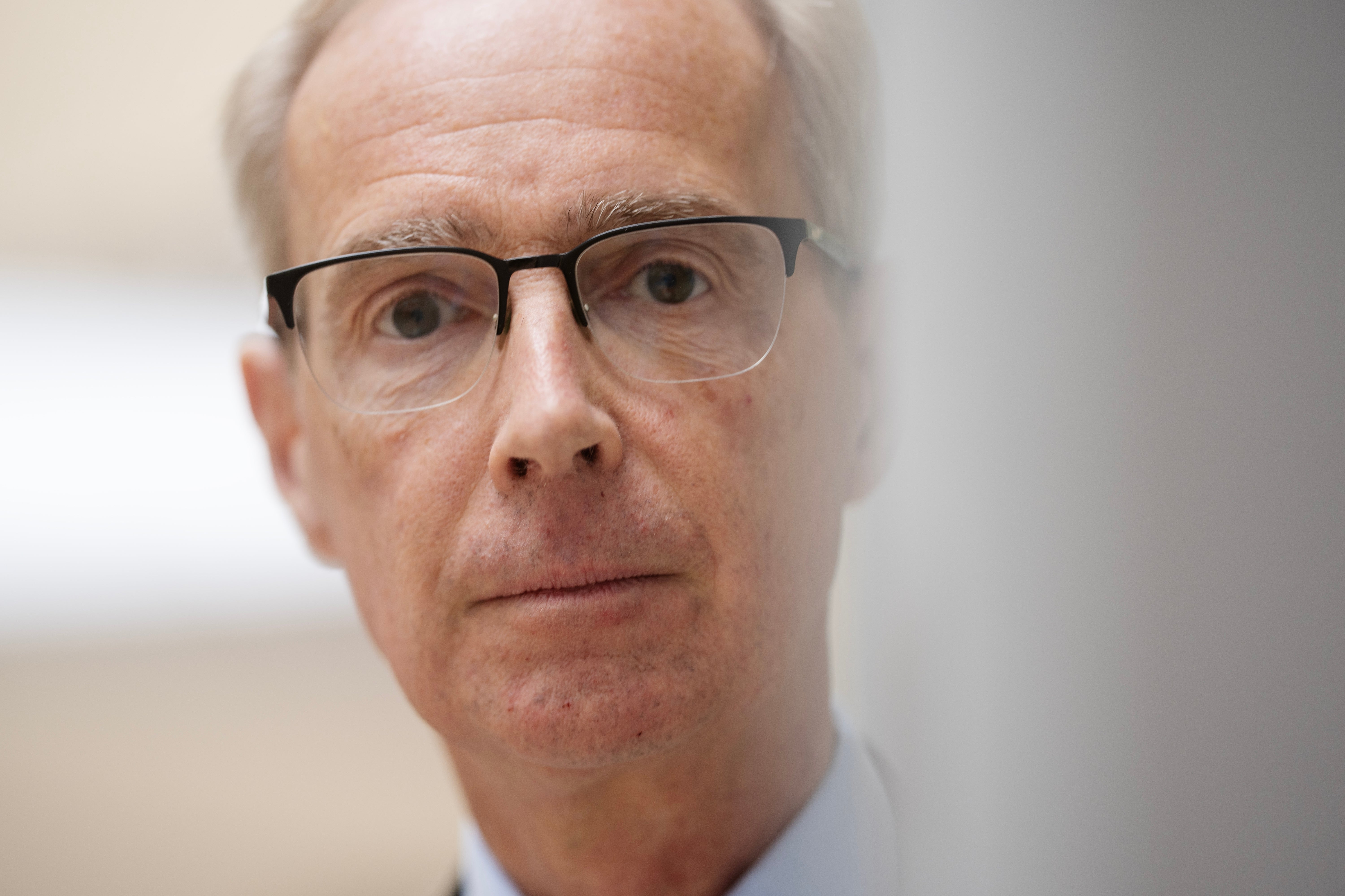 Porträtt av en äldre man med glasögon och vit hår som tittar direkt in i kameran.