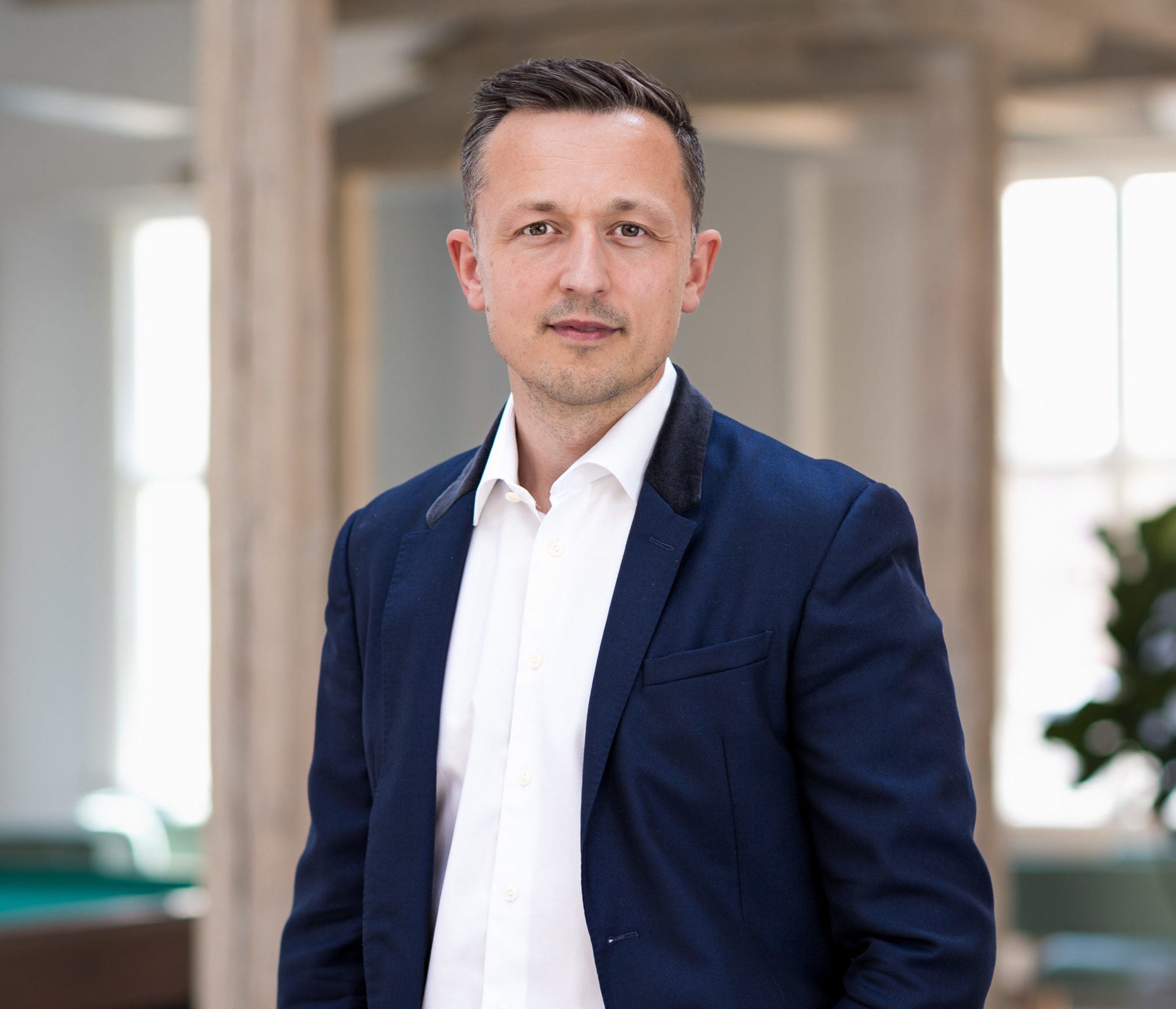 Porträtt av en man i mörkblå kavaj och vit skjorta i en modern kontorsmiljö.