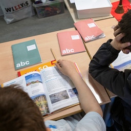 Två elever sitter vid ett bord i klassrummet och läser tillsammans i en tidskrift. Läroböcker ligger på bordet runt omkring dem.