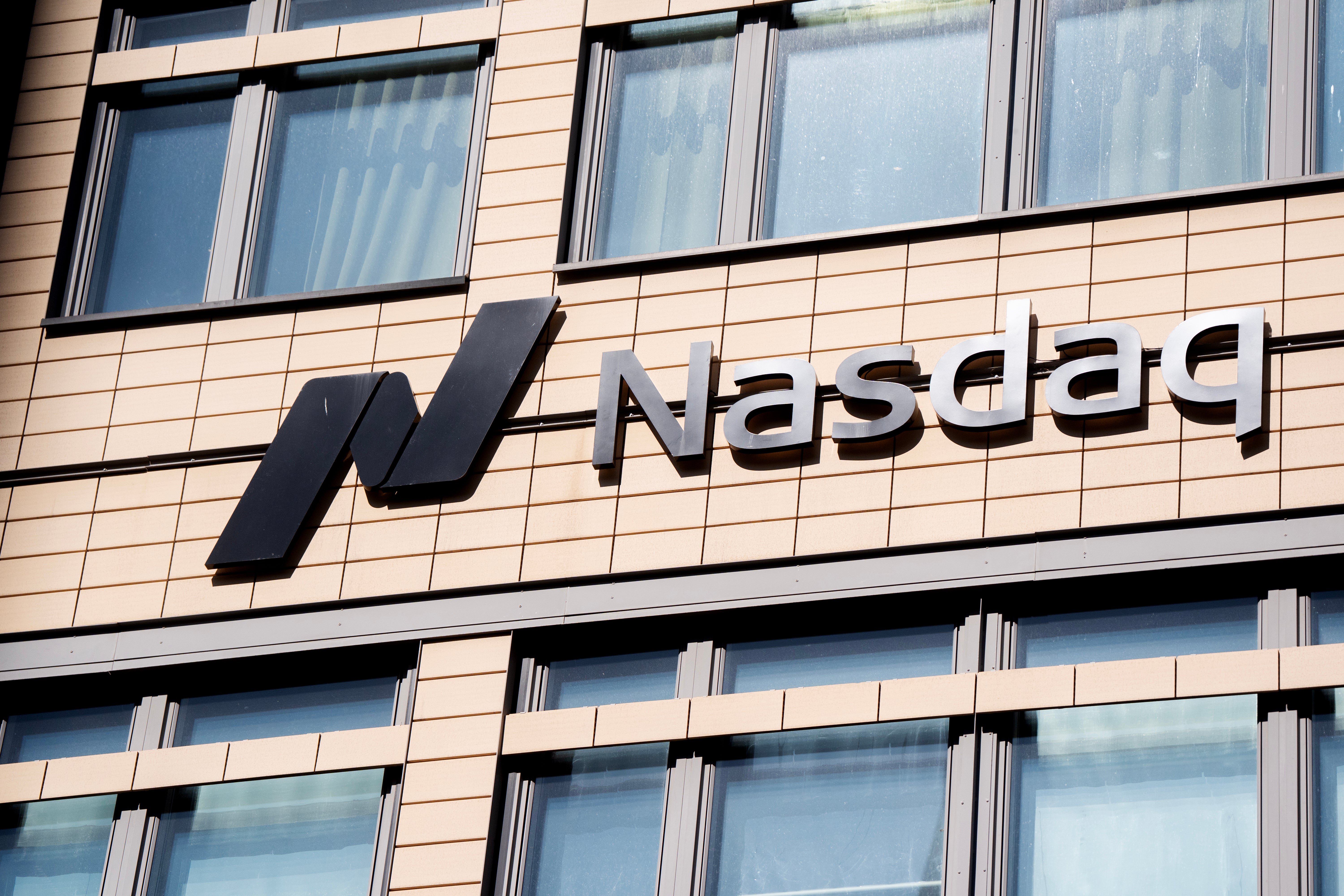 Nasdaqs logotyp på fasaden av en kontorsbyggnad med ljus tegelbeklädnad och fönster.
