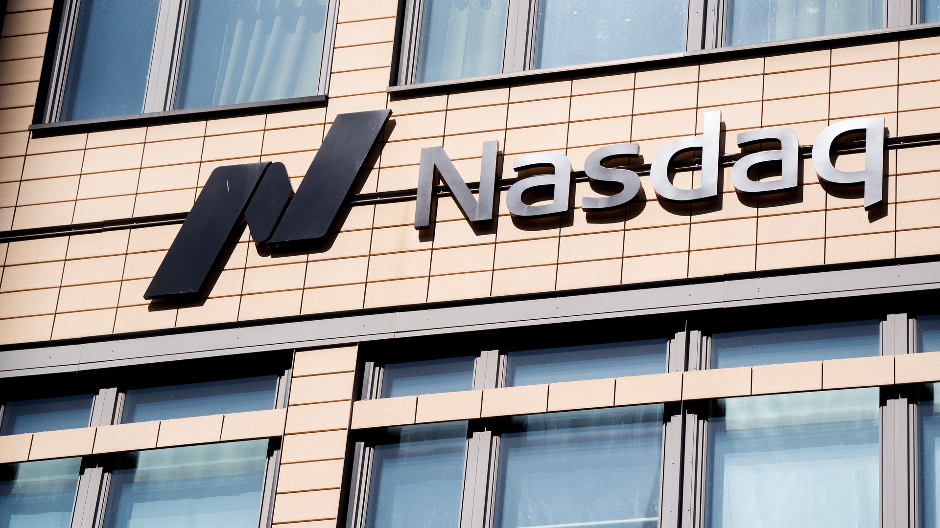 Nasdaqs logotyp på fasaden av en kontorsbyggnad med ljus tegelbeklädnad och fönster.