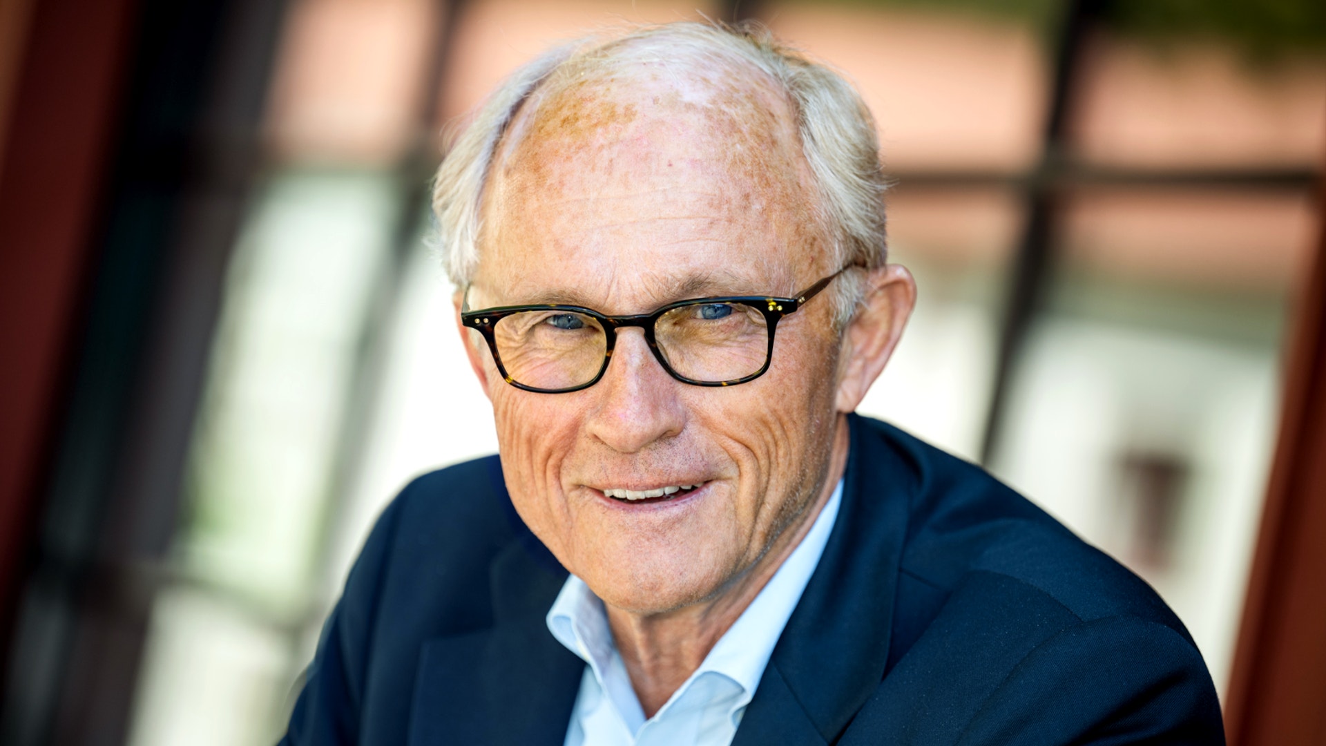 Porträtt av en äldre man med glasögon som ler mot kameran