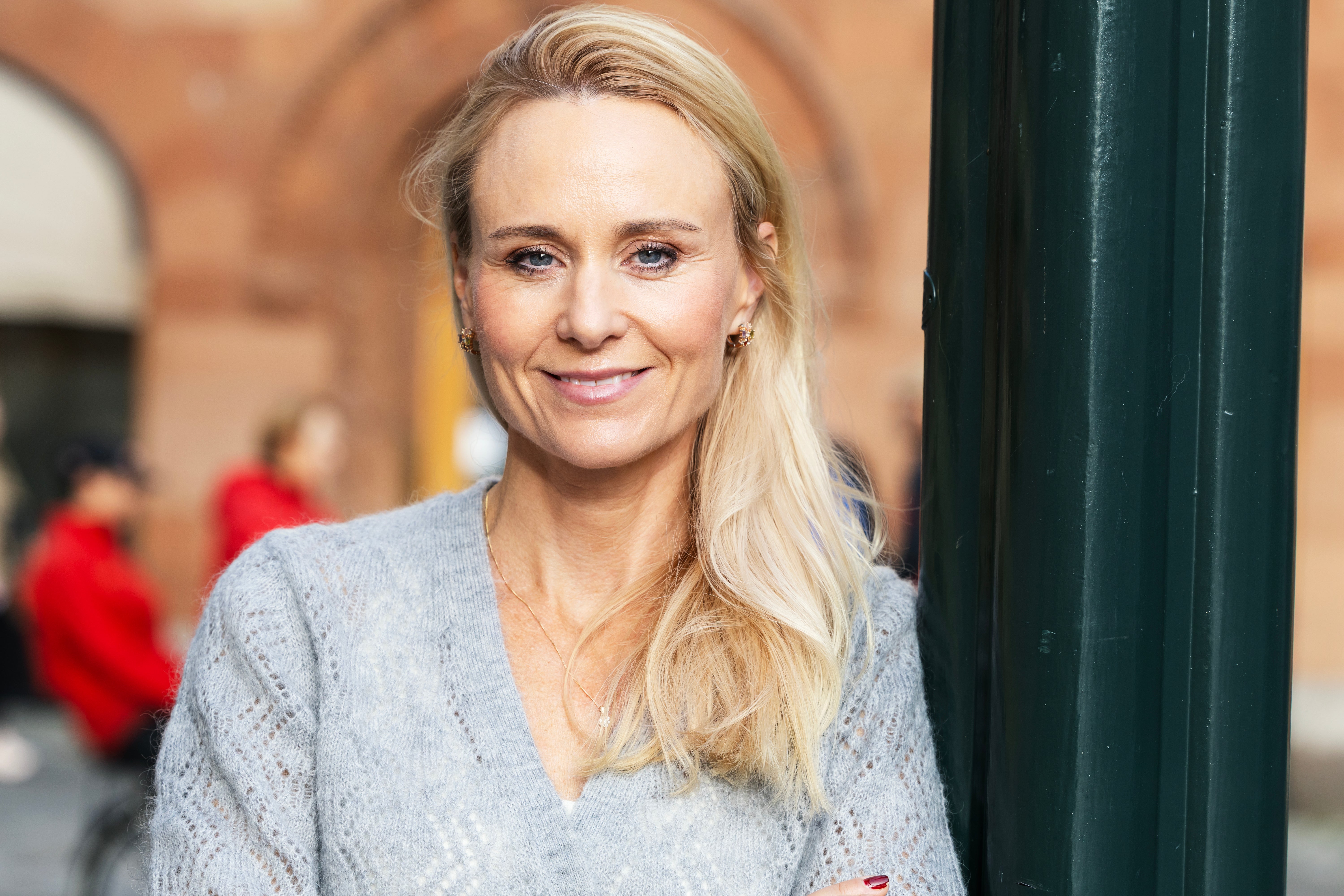 En leende kvinna med blont hår står utomhus i en stickad tröja.
