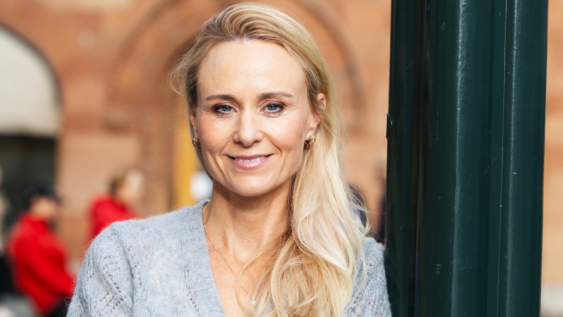En leende kvinna med blont hår står utomhus i en stickad tröja.