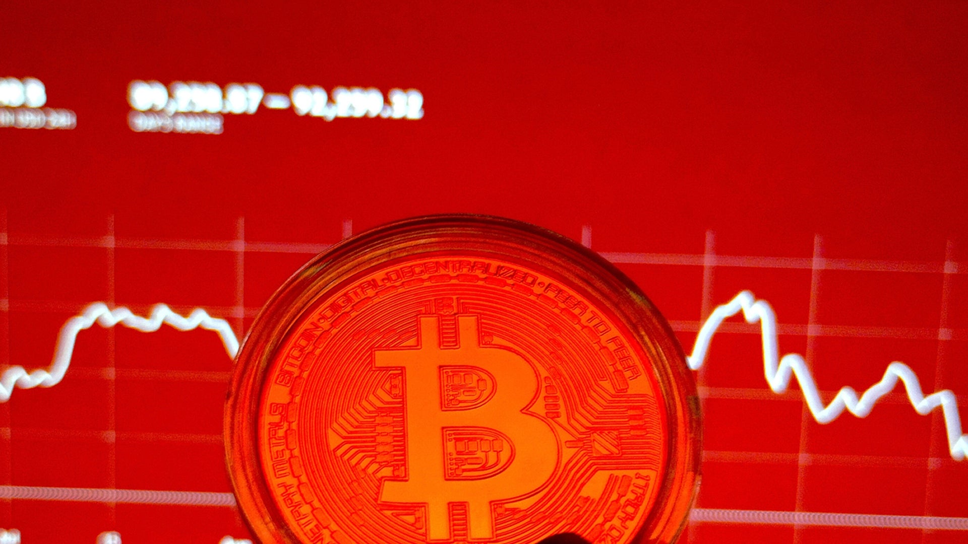 En glödande Bitcoin-mynt framför ett rött diagram med en fallande kurva som visar prisfall.