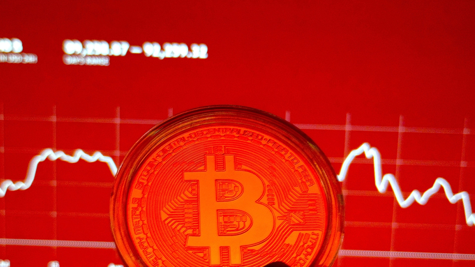 En glödande Bitcoin-mynt framför ett rött diagram med en fallande kurva som visar prisfall.