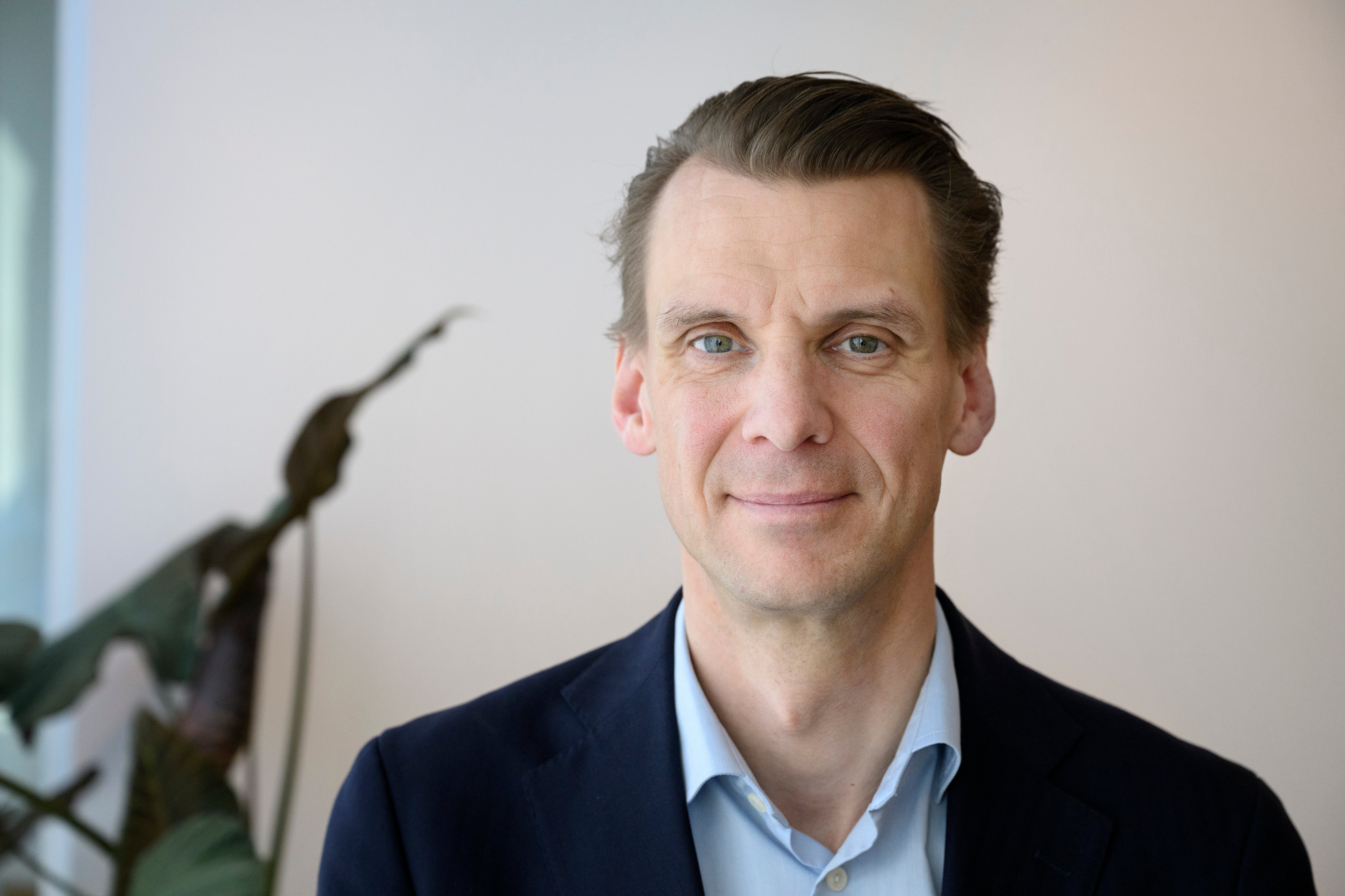 Porträttfoto av en man i mörkblå kavaj och ljusblå skjorta mot en ljus bakgrund.