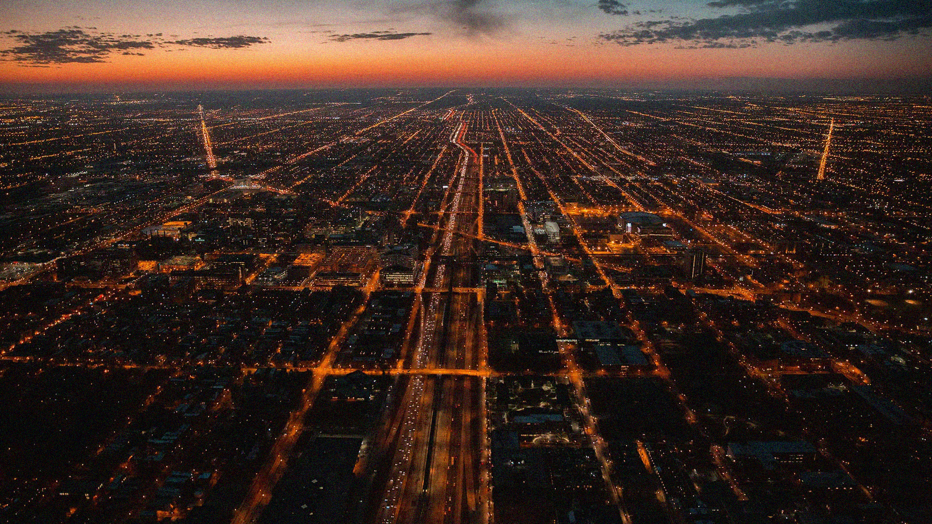 Flygfoto över en stad vid skymning med upplysta gator och motorvägar som bildar ett rutnätsmönster