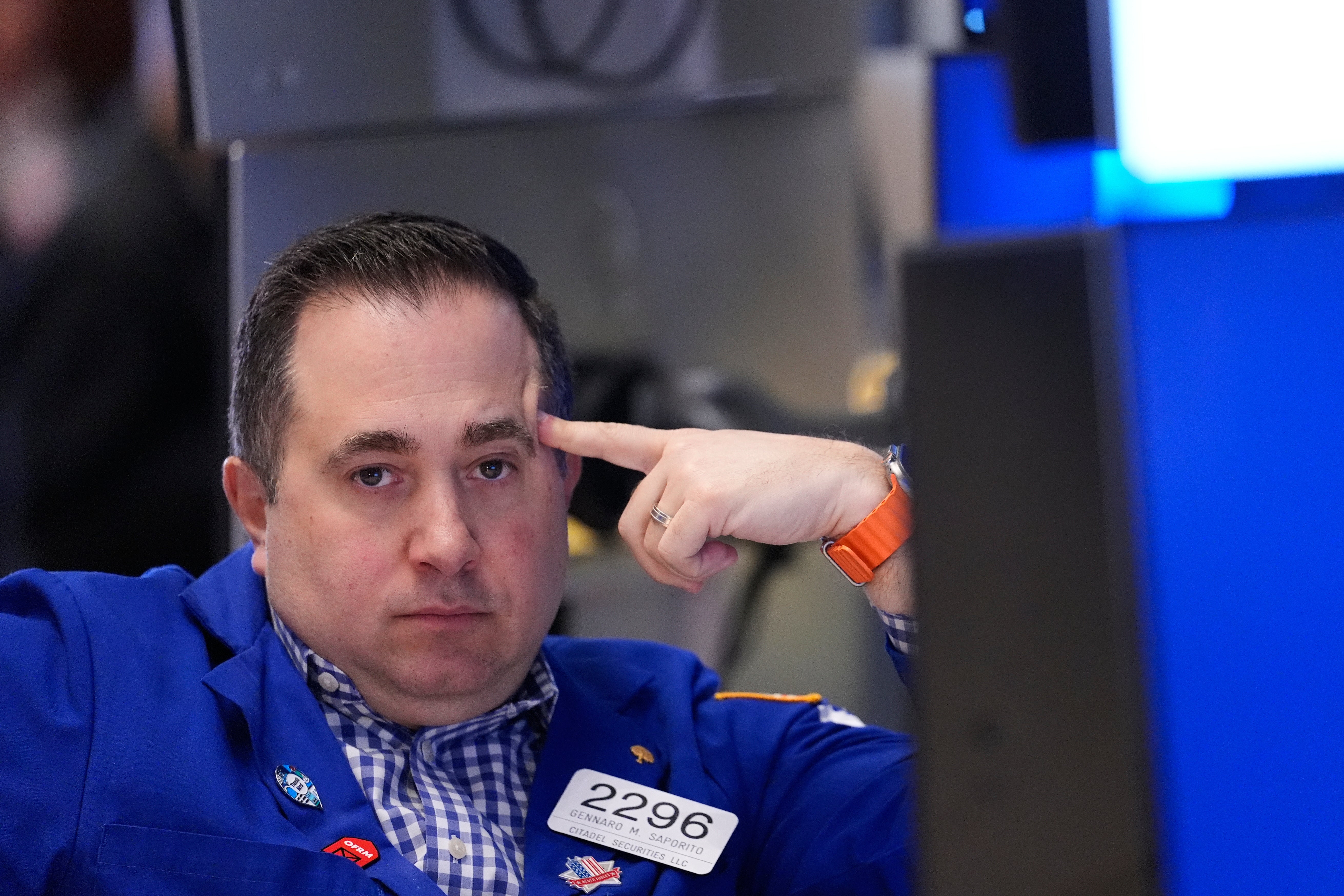 Man i blå jacka med namnbricka gör en tankefull gest mot sitt huvud