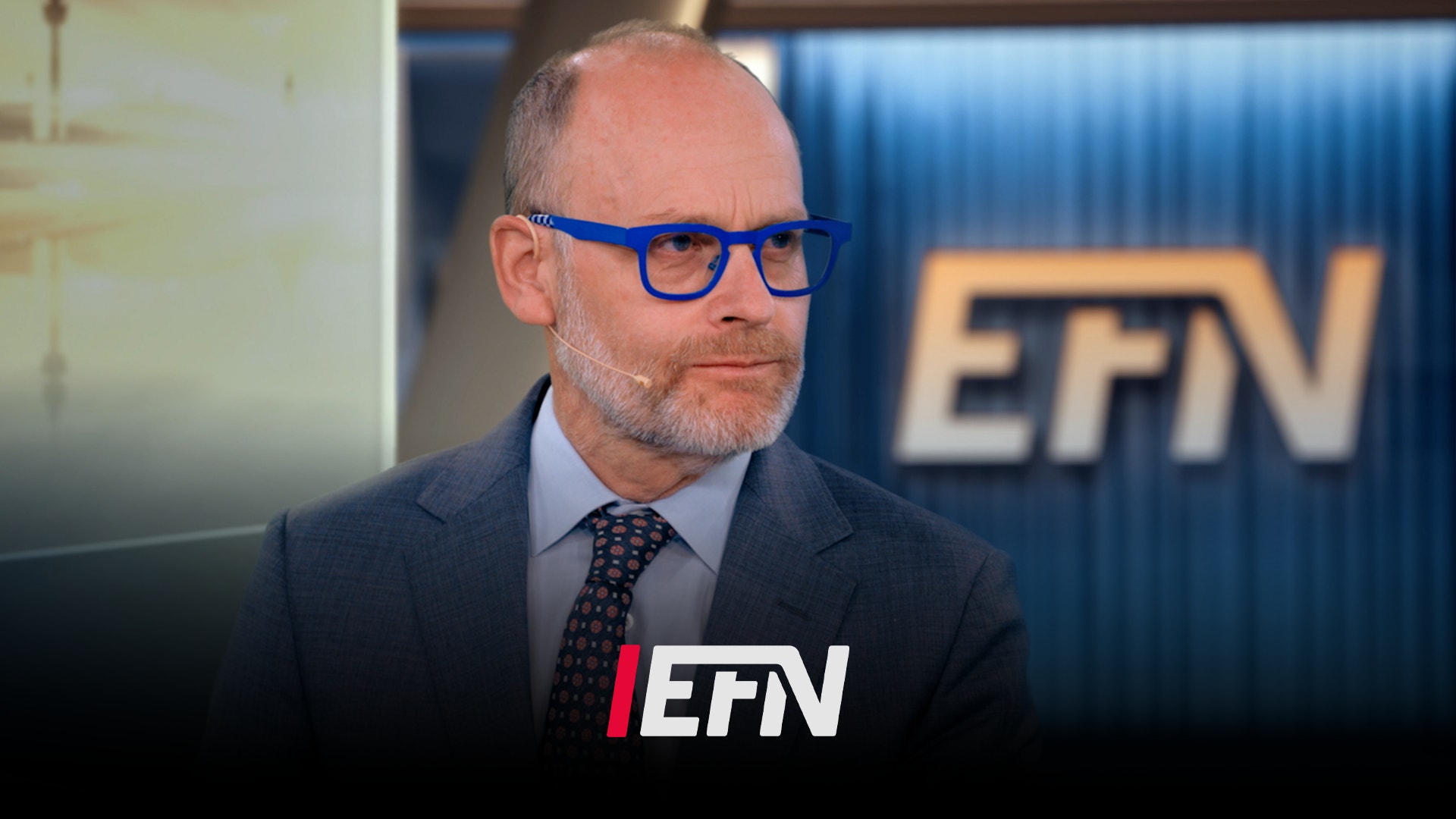 En man med blå glasögon och mörk kostym framför en EFN-bakgrund.