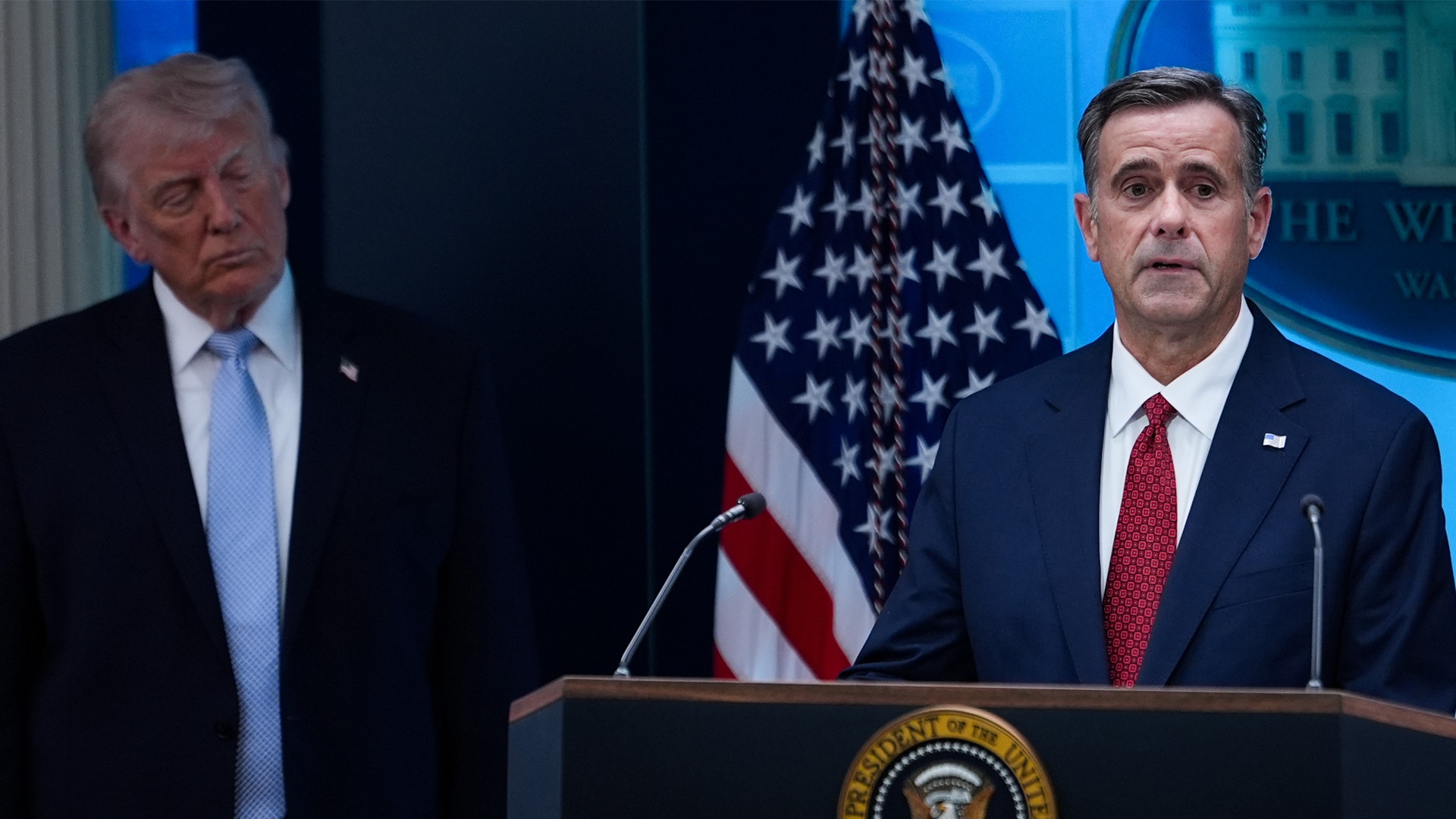 Två män i kostym vid ett presidentiellt podium framför en amerikansk flagga under en officiell presskonferens.