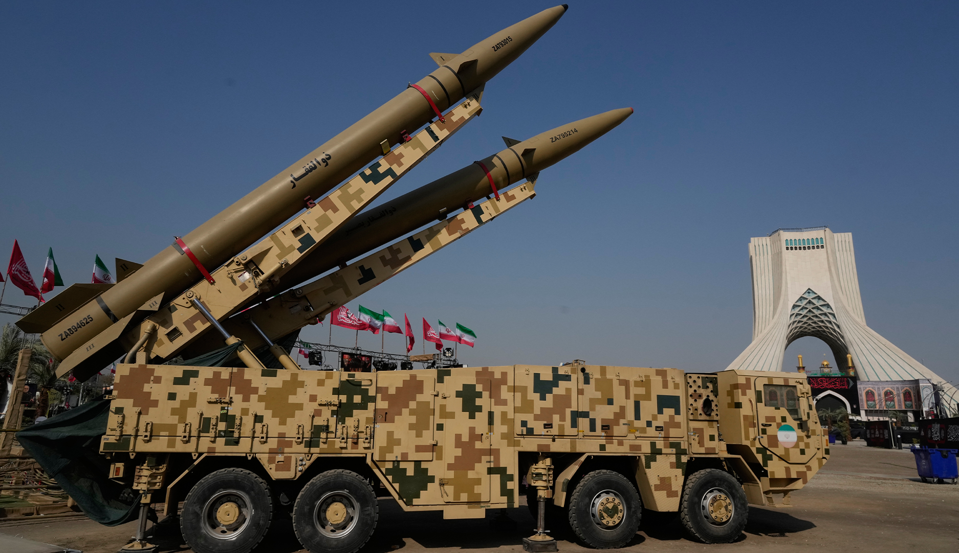 Två missiler på en militär lastbil utställda utomhus, med Azadi-tornet i Teheran i bakgrunden.
