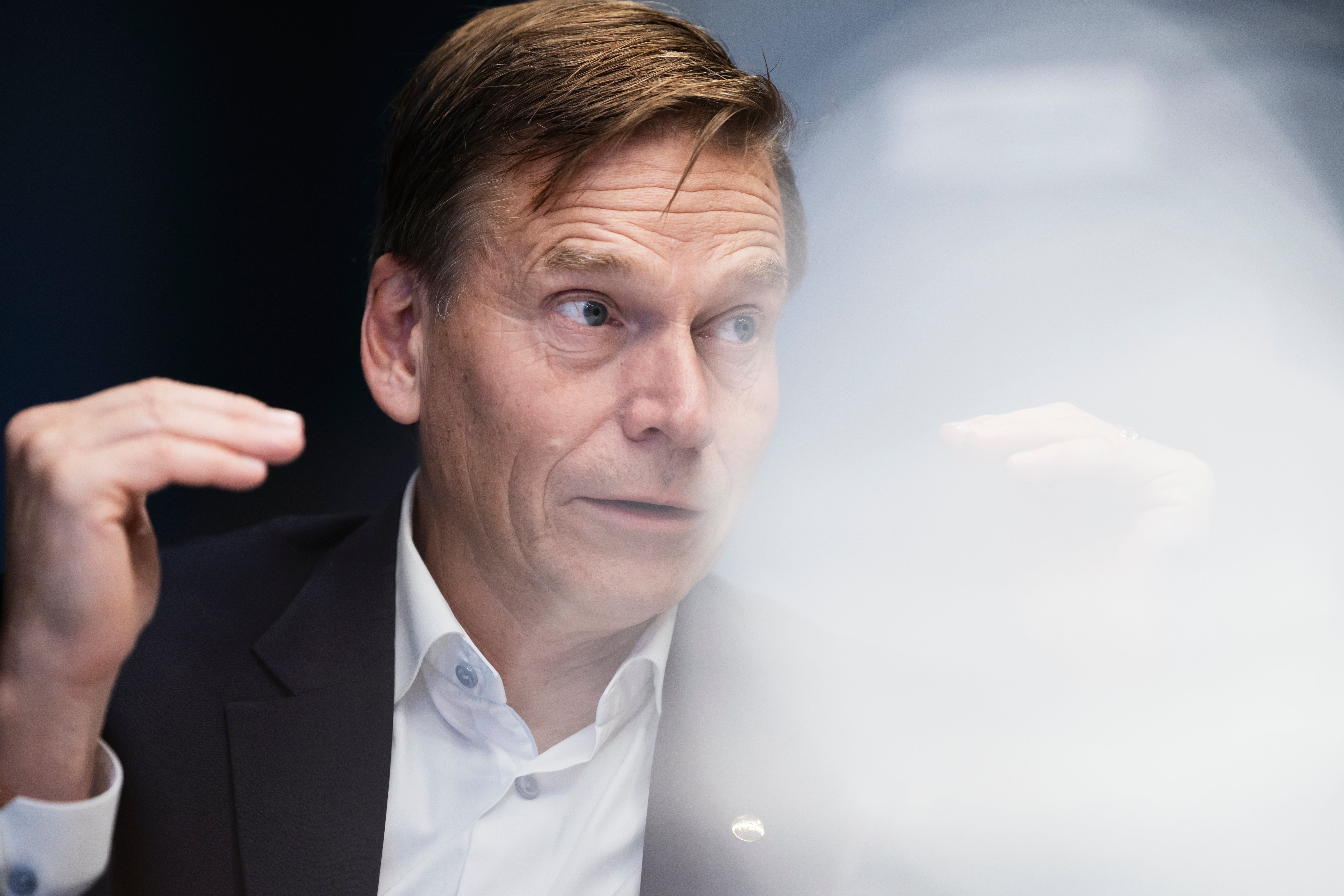 En man i kostym och vit skjorta gestikulerar med handen medan han pratar.