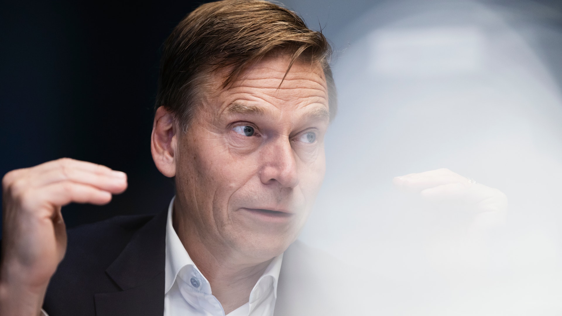 En man i kostym och vit skjorta gestikulerar med handen medan han pratar.