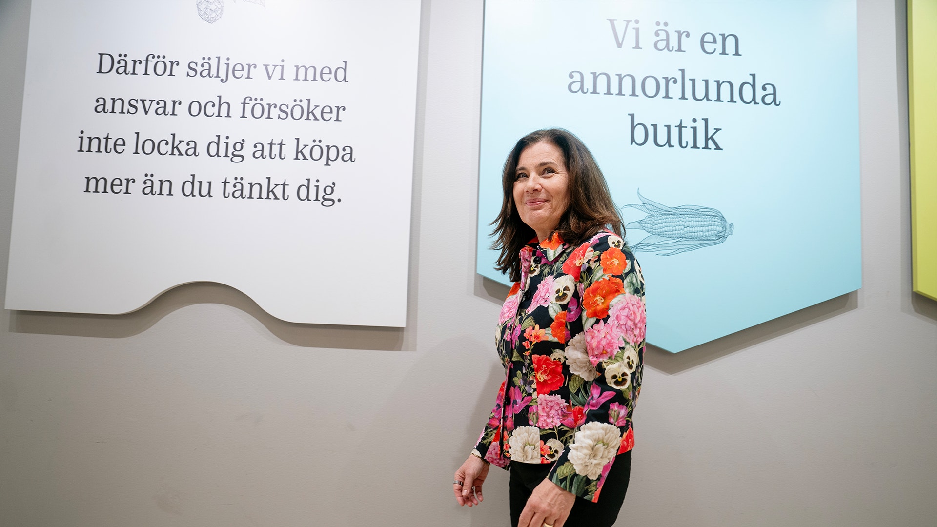 Ann Carlsson Meyer går framför Systembolagets flertal budskap på väggarna. På en av de står det "Vi är en annorlunda butik".