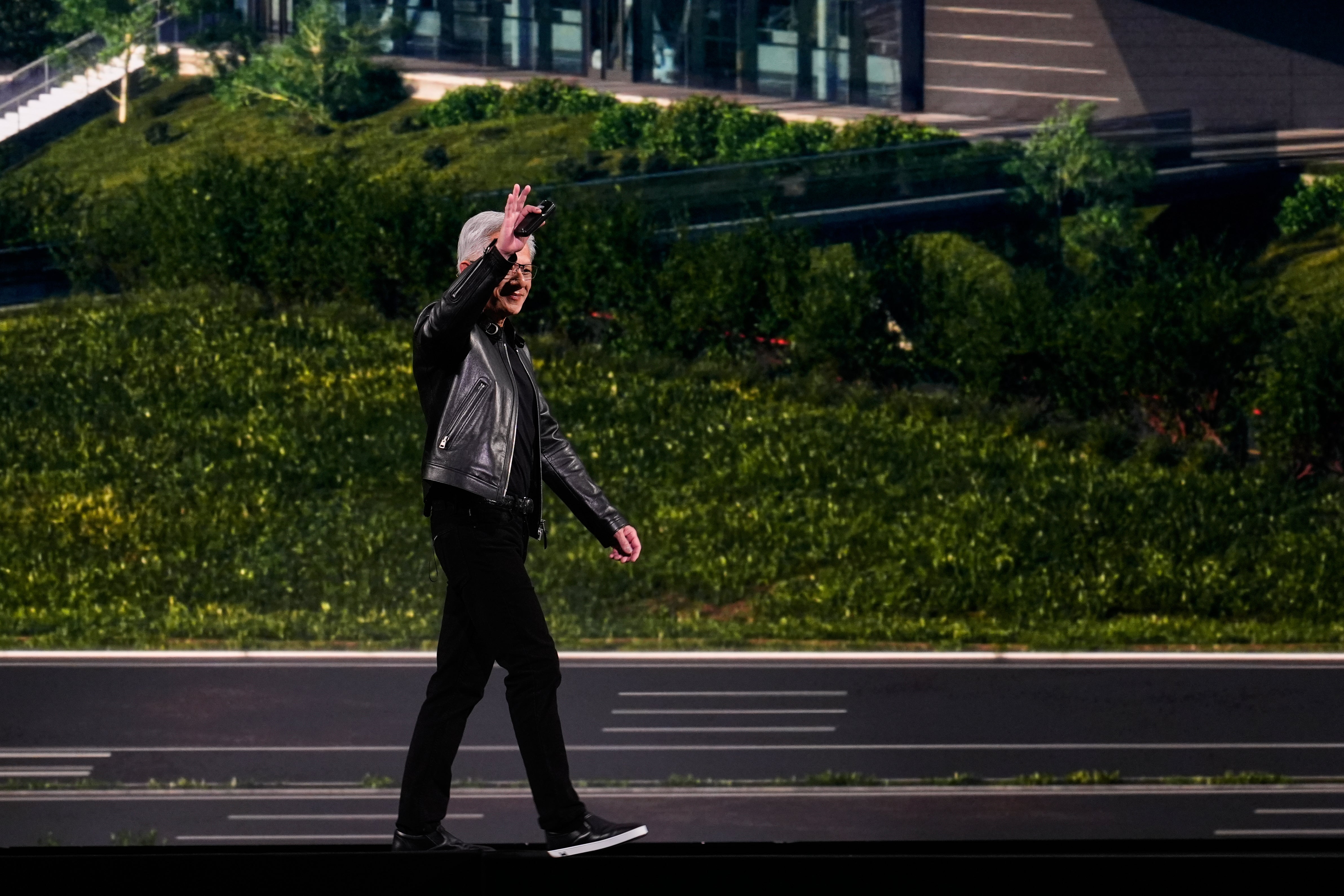 Person i svart jacka går på en stadsgata med gröna växter och moderna byggnader i bakgrunden.