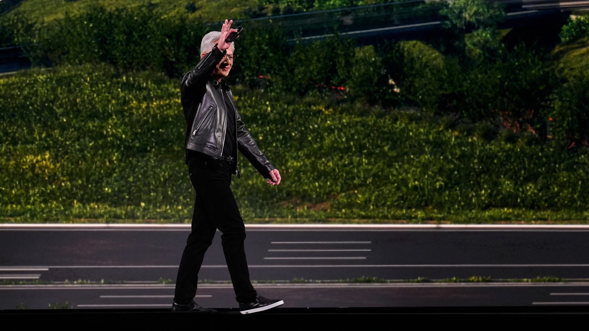 Person i svart jacka går på en stadsgata med gröna växter och moderna byggnader i bakgrunden.