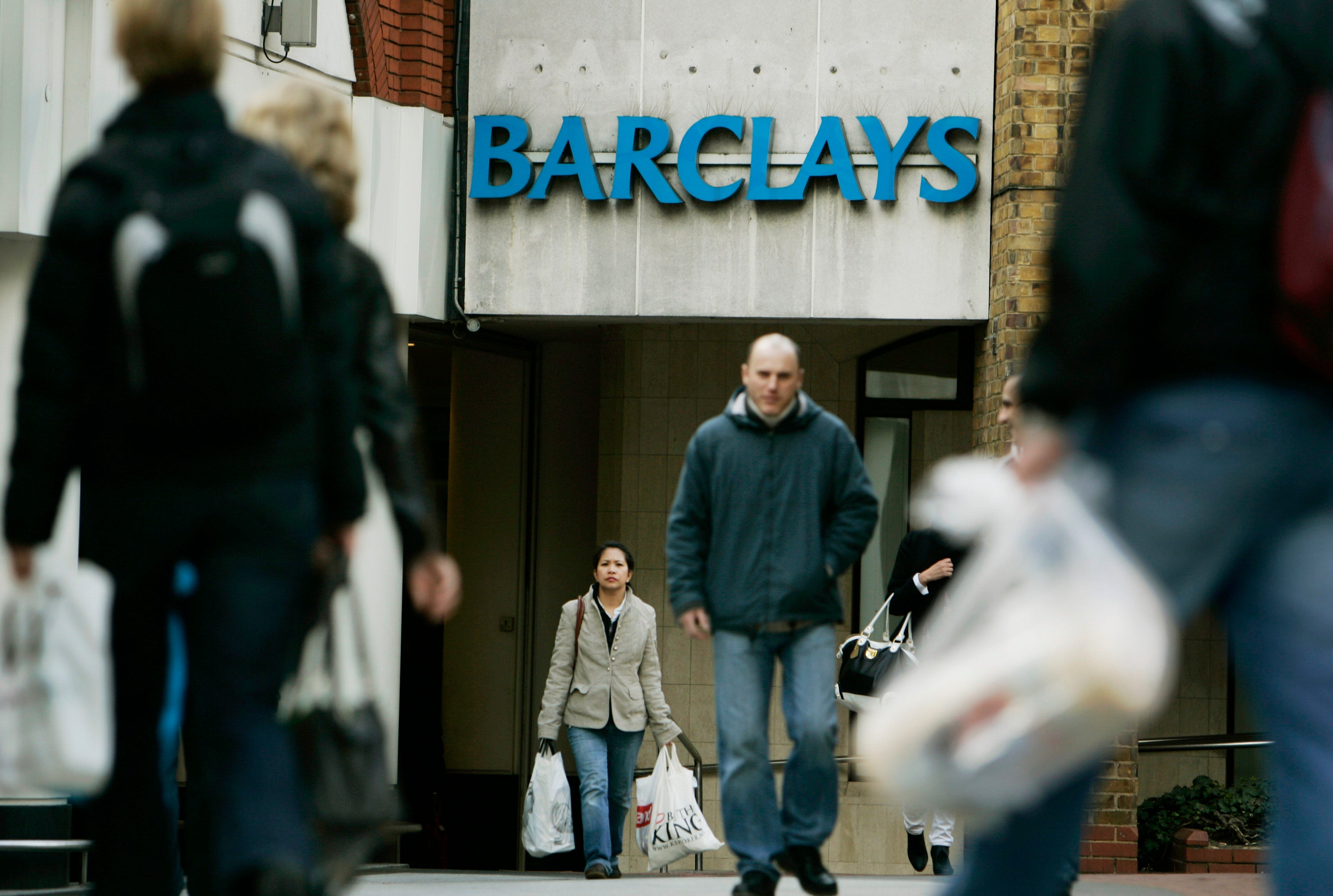 Människor med shoppingkassar går förbi en bankkontor med Barclays-skylt.