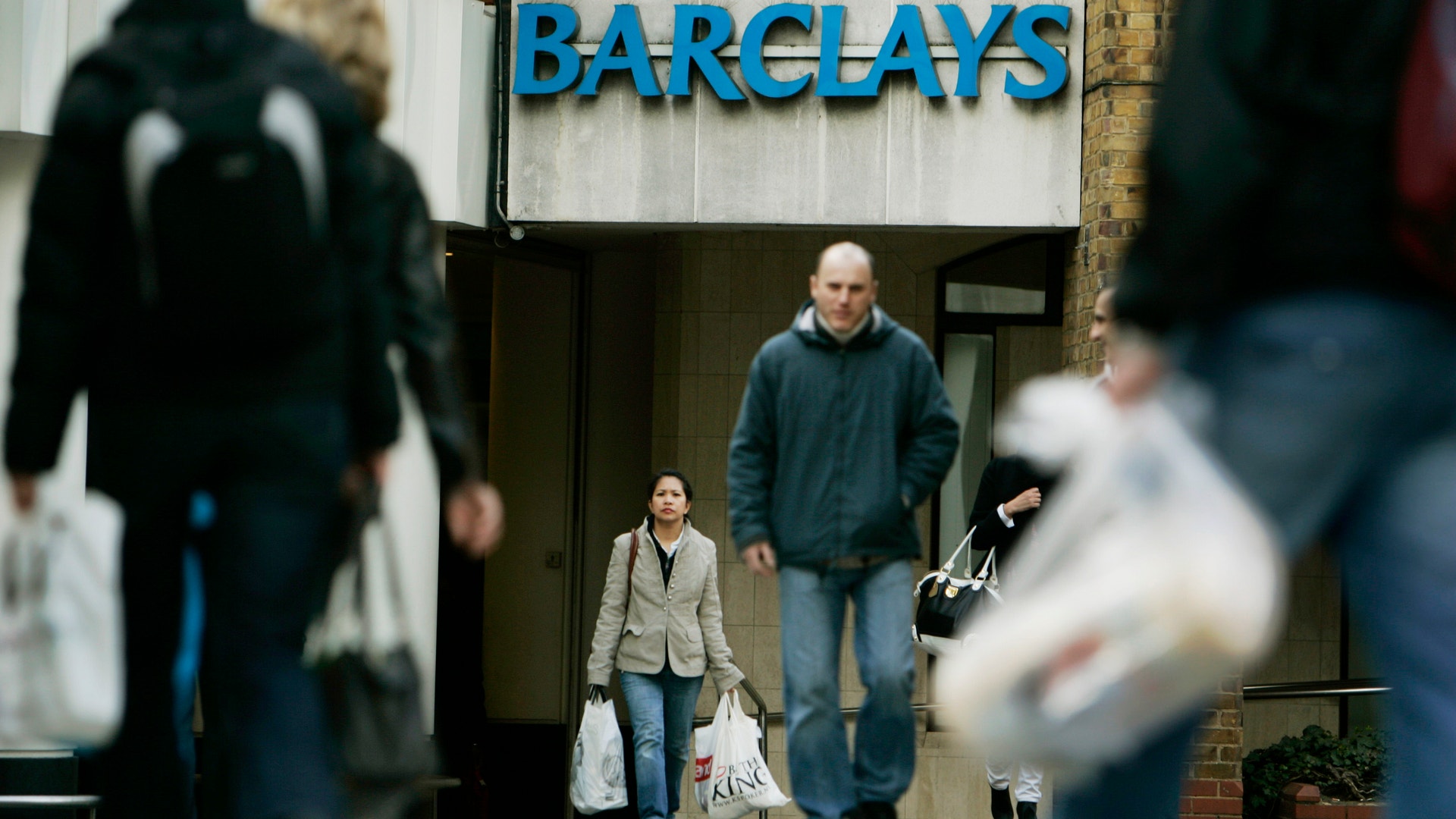 Människor med shoppingkassar går förbi en bankkontor med Barclays-skylt.
