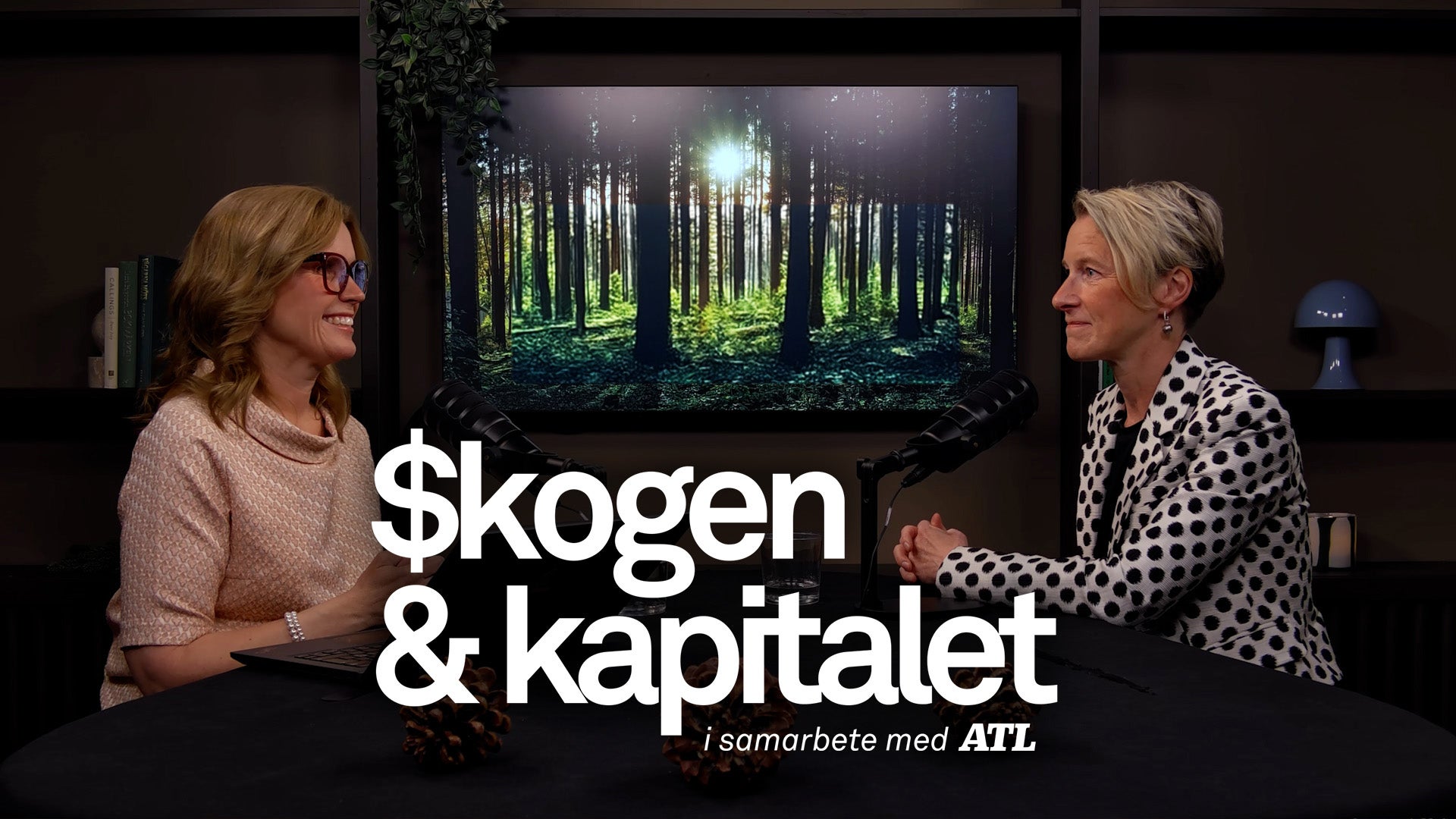 Två kvinnor i samtal framför en skärm som visar en grön skog. Text på bilden säger "$kogen & kapitalet i samarbete med AIL".