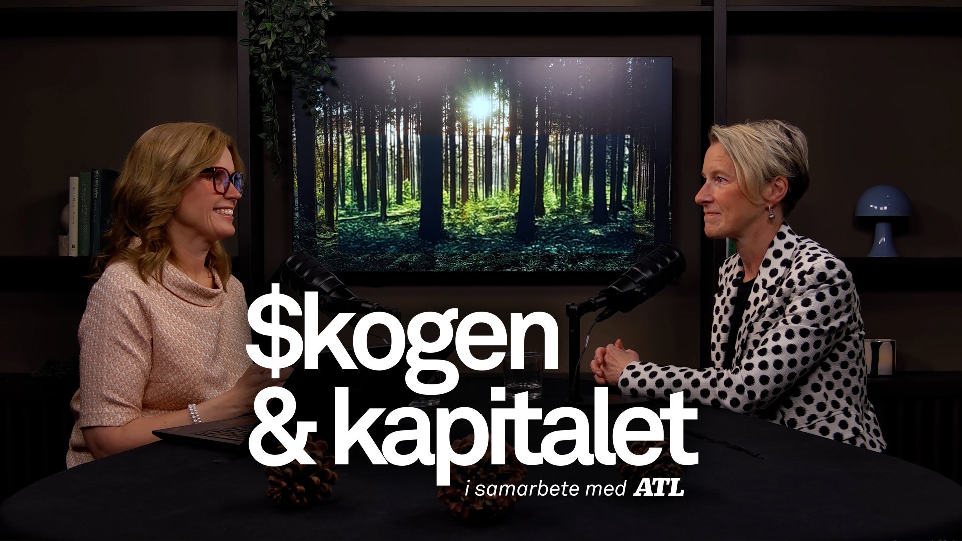 Två kvinnor i samtal framför en skärm som visar en grön skog. Text på bilden säger "$kogen & kapitalet i samarbete med AIL".