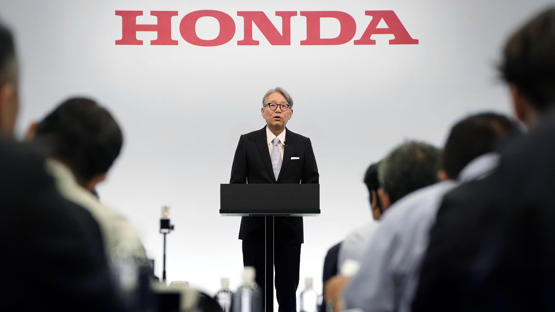 Man i kostym står vid ett podium under Honda-loggan och presenterar för en publik.