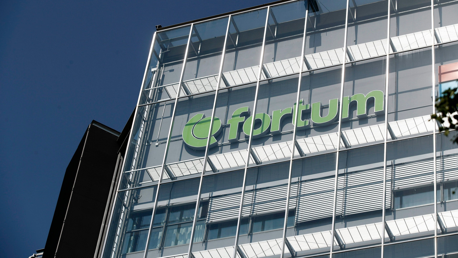 Modern kontorsbyggnad med glasfasad och grön text på fasaden mot blå himmel.
