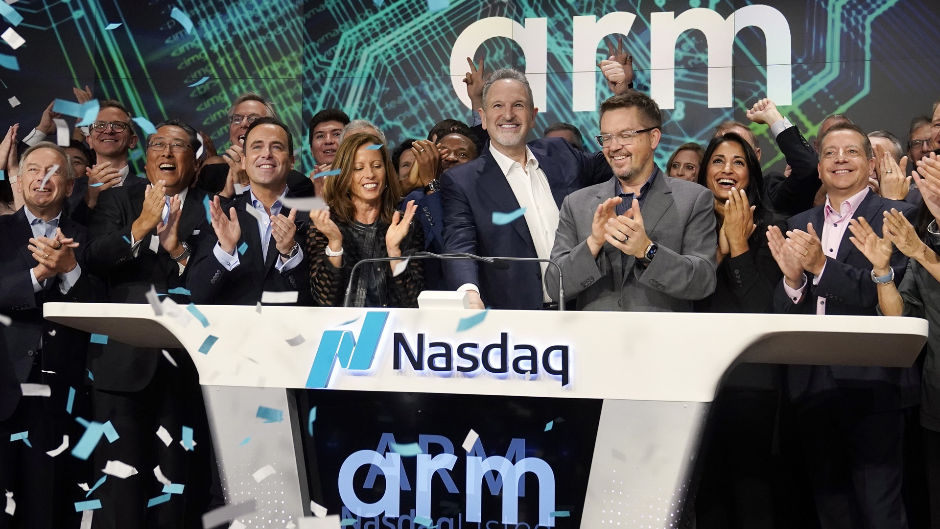 En grupp affärspersoner applåderar vid en Nasdaq-börsceremoni med ARM-logotyper synliga i bakgrunden.