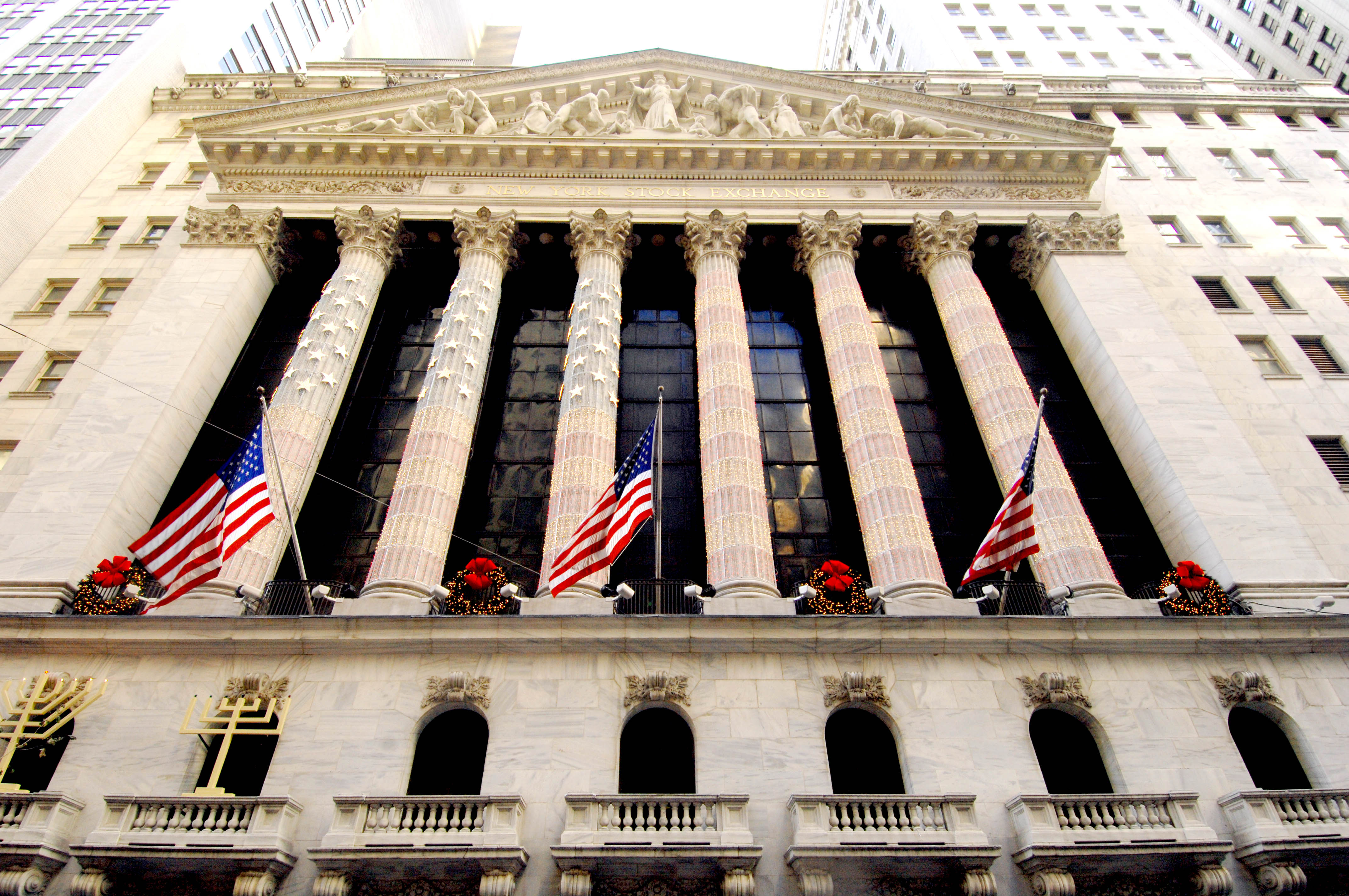 Fasaden på börshuset New York Stock Exchange på Wall Street med höga kolonner och amerikanska flaggor, sedd underifrån.