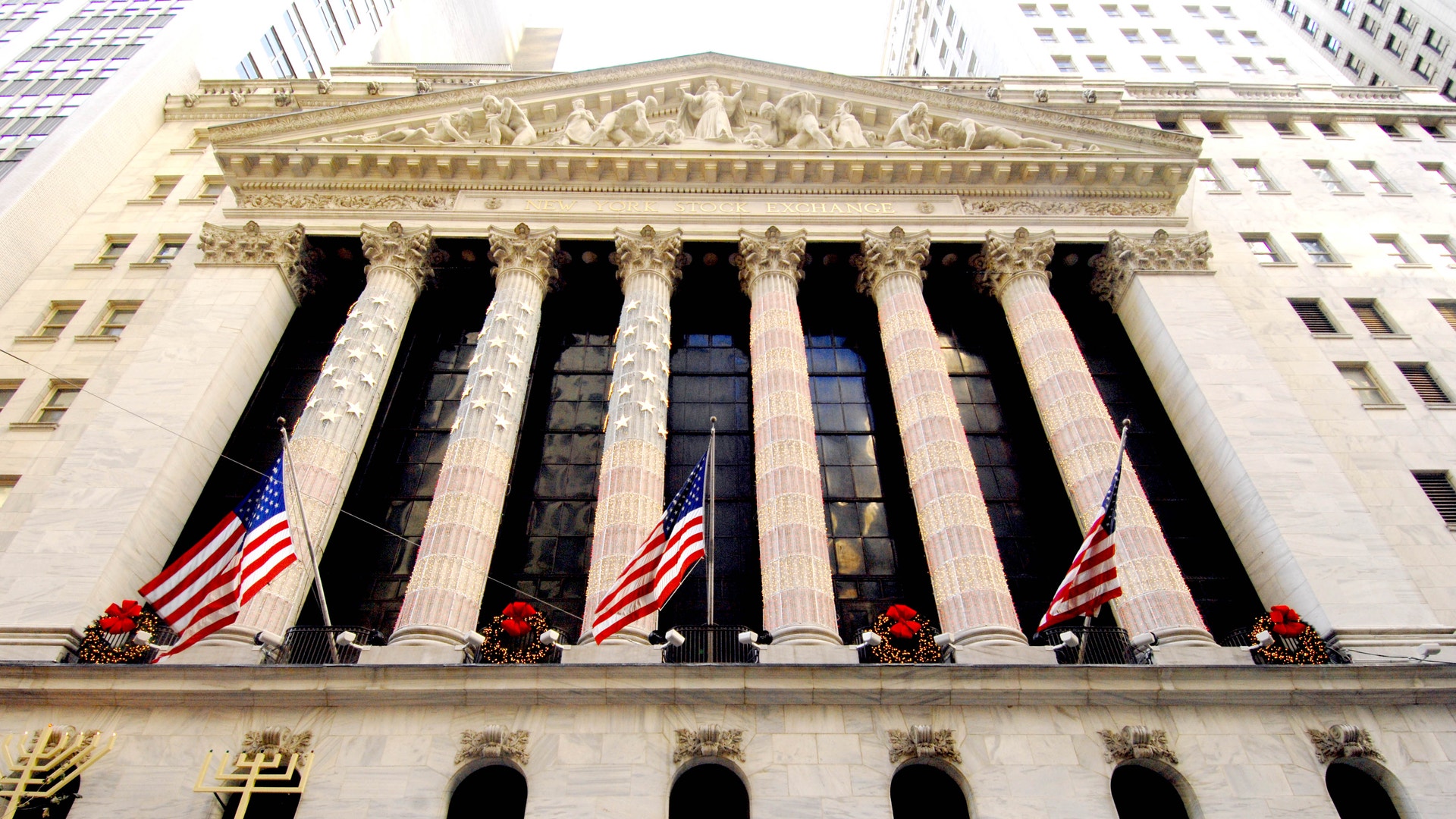 Fasaden på börshuset New York Stock Exchange på Wall Street med höga kolonner och amerikanska flaggor, sedd underifrån.